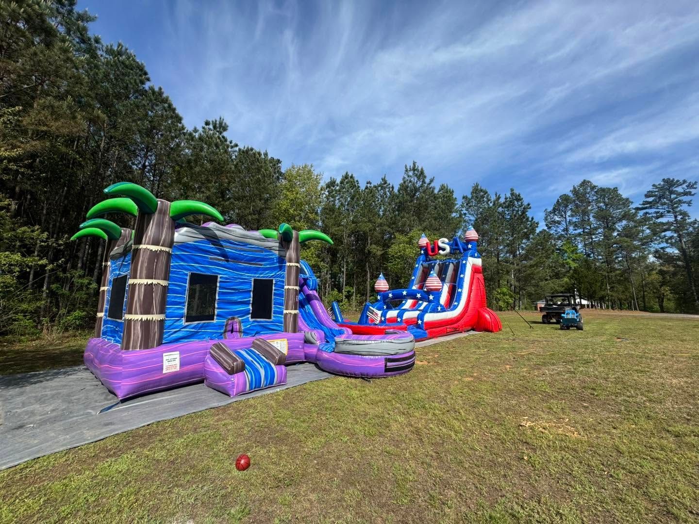 Colorful inflatable bounce house and slide setup on a grassy field with trees in the background