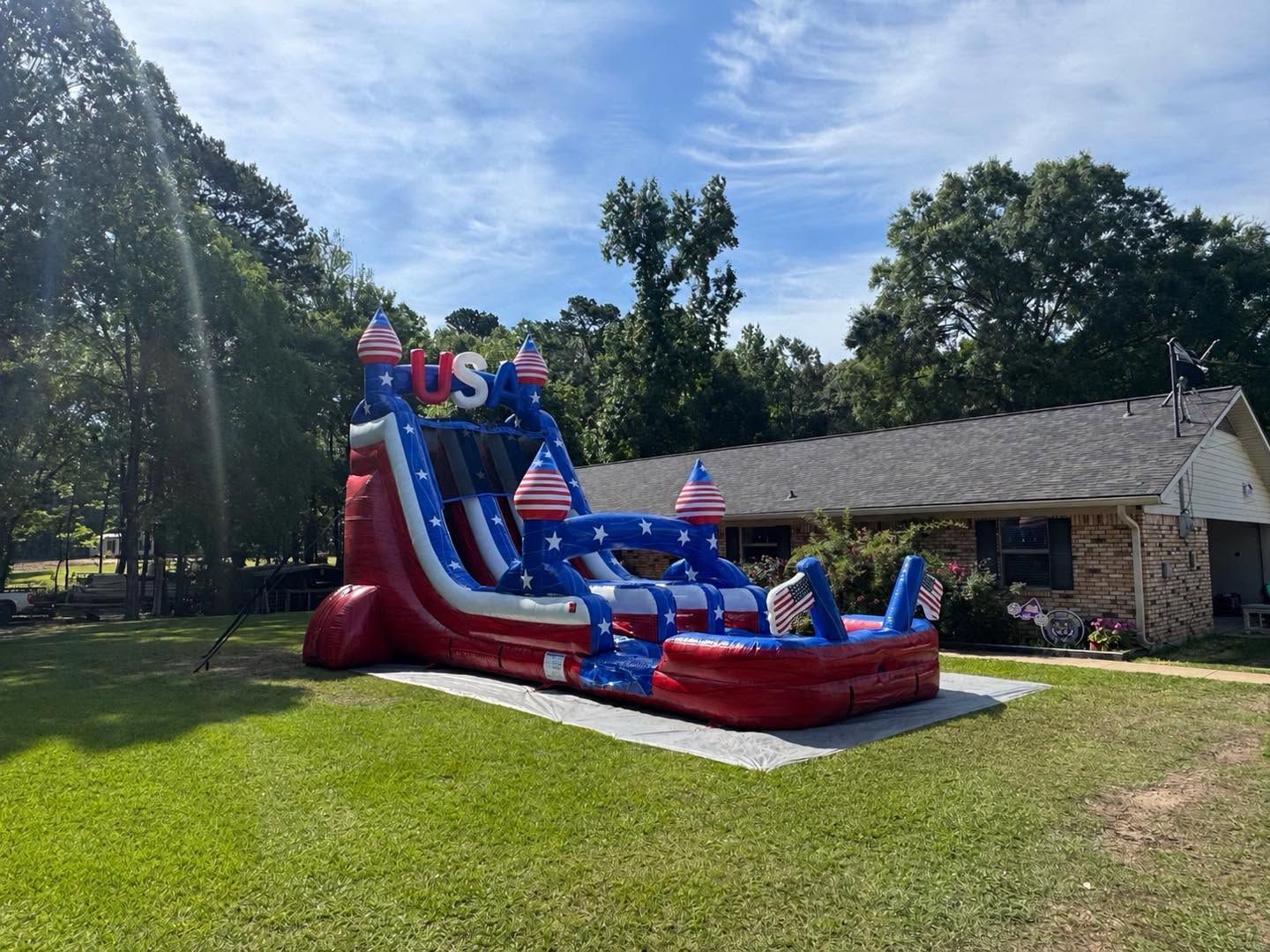 Red, white, and blue inflatable slide on a lawn beside a stone building under sunny skies