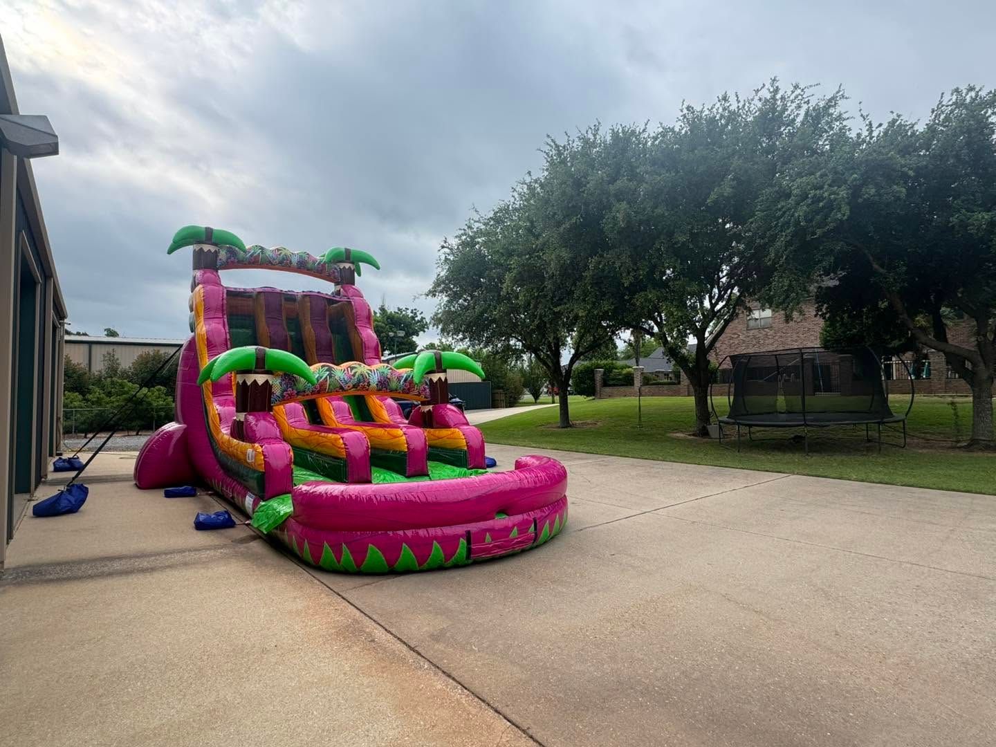 Colorful inflatable water slide beside a house on a driveway under cloudy skies.