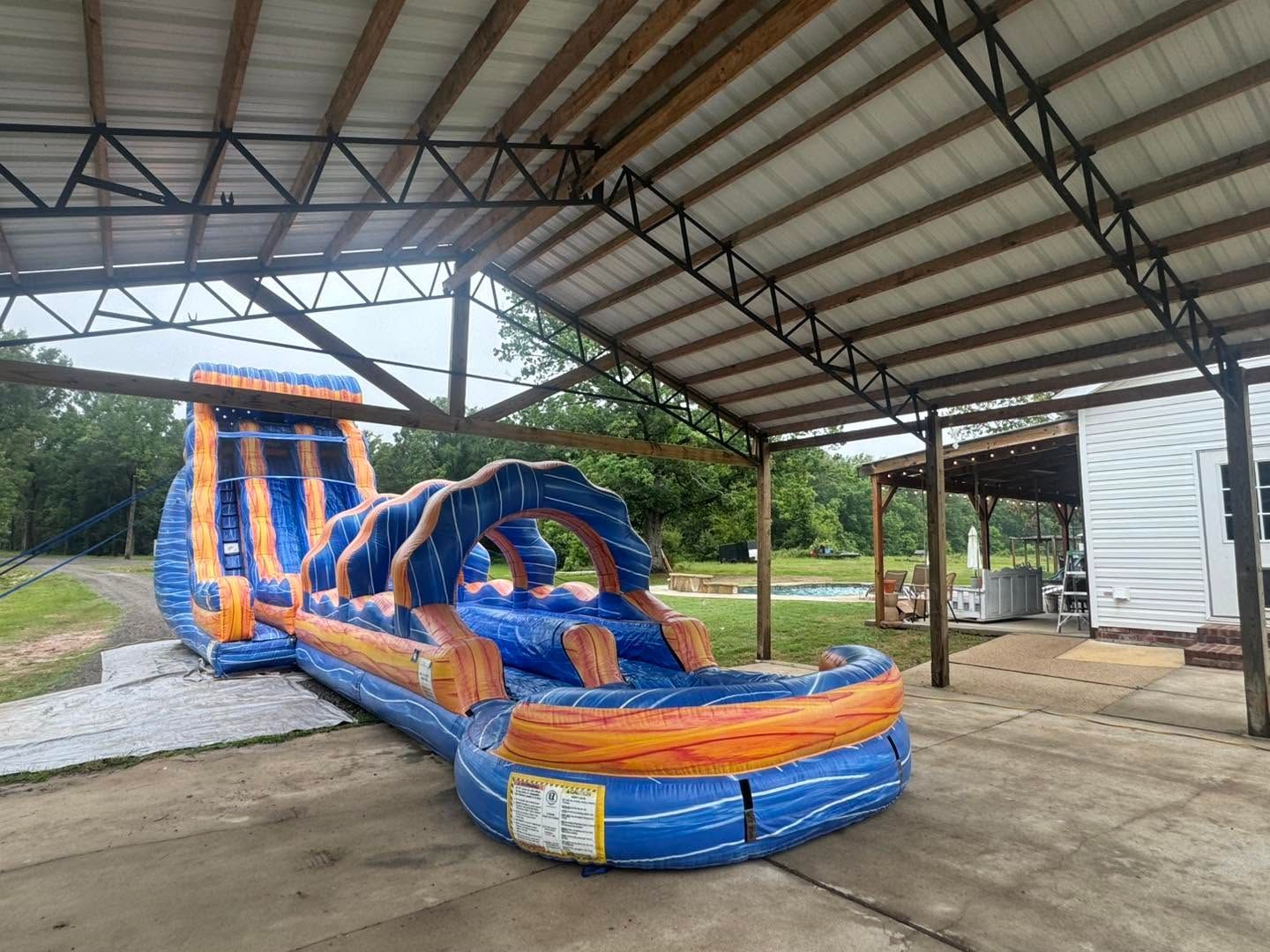 Blue and orange inflatable obstacle course under a covered pavilion on a concrete floor
