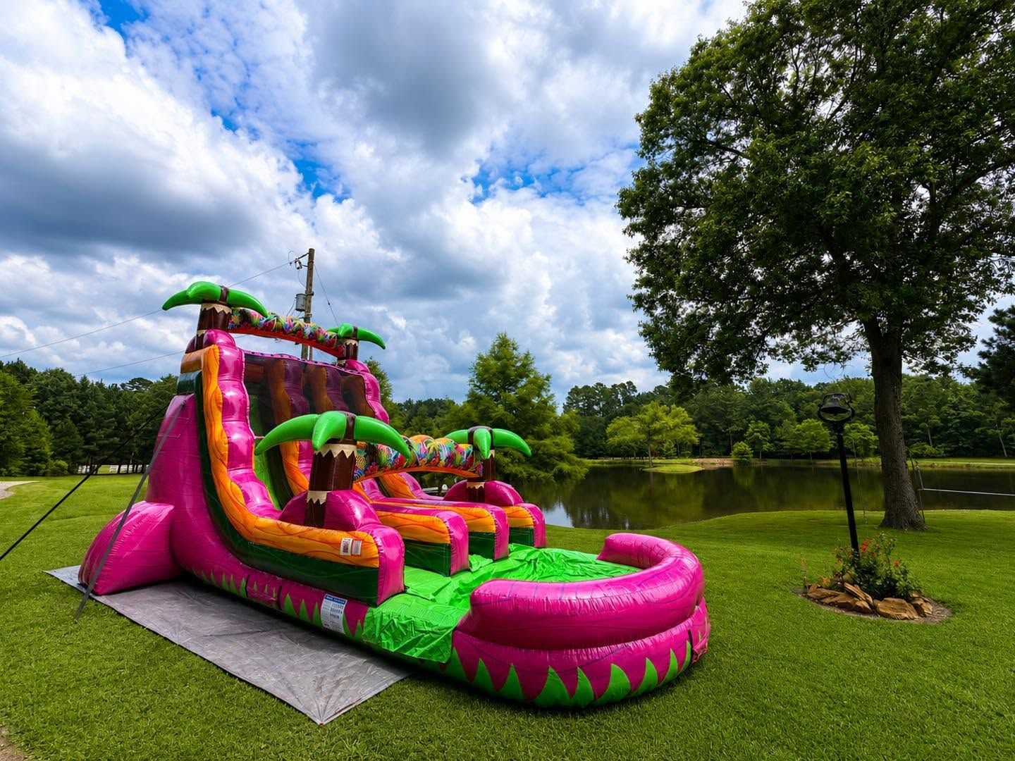 Bright pink and green inflatable slide in a grassy park under a cloudy sky