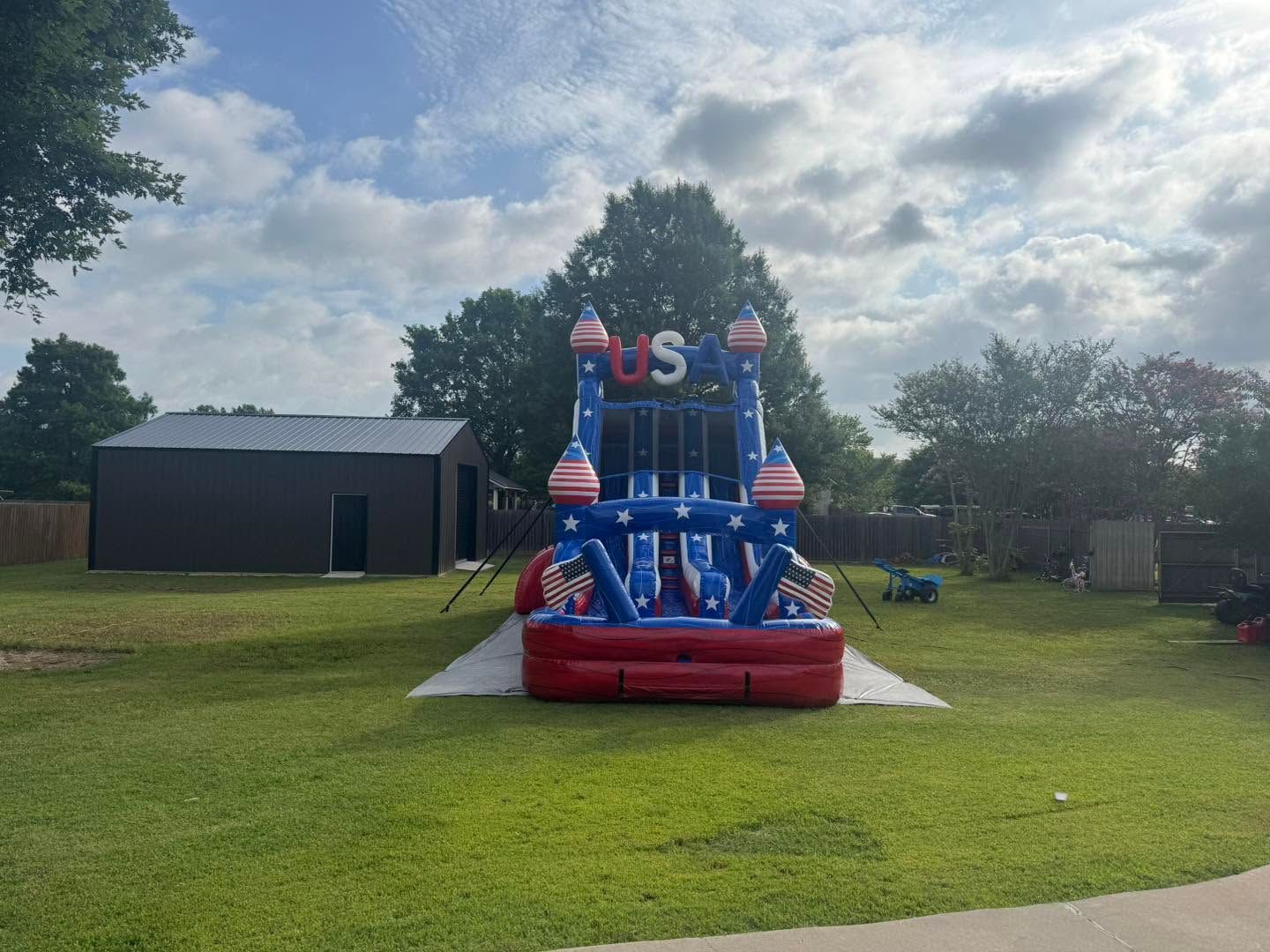 Blue and red inflatable bounce house on a lawn with a cloudy sky overhead