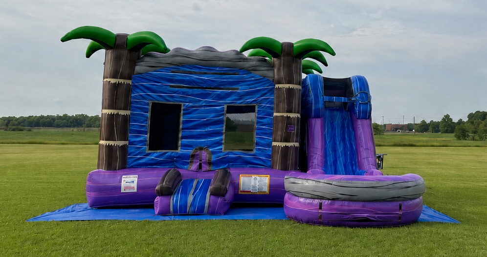 Blue and purple inflatable bounce house with palm trees and slide on a grassy field