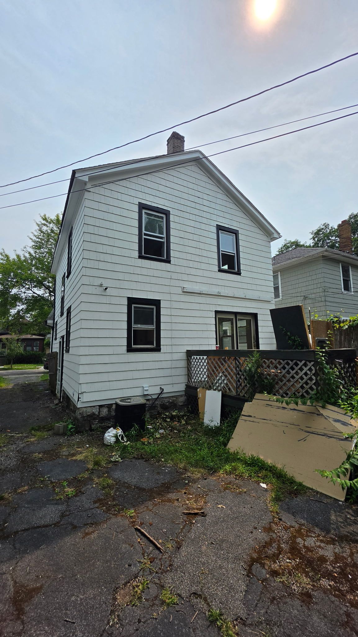 White two-story house with black-trimmed windows and a small porch in a wet driveway, seen from the yard.