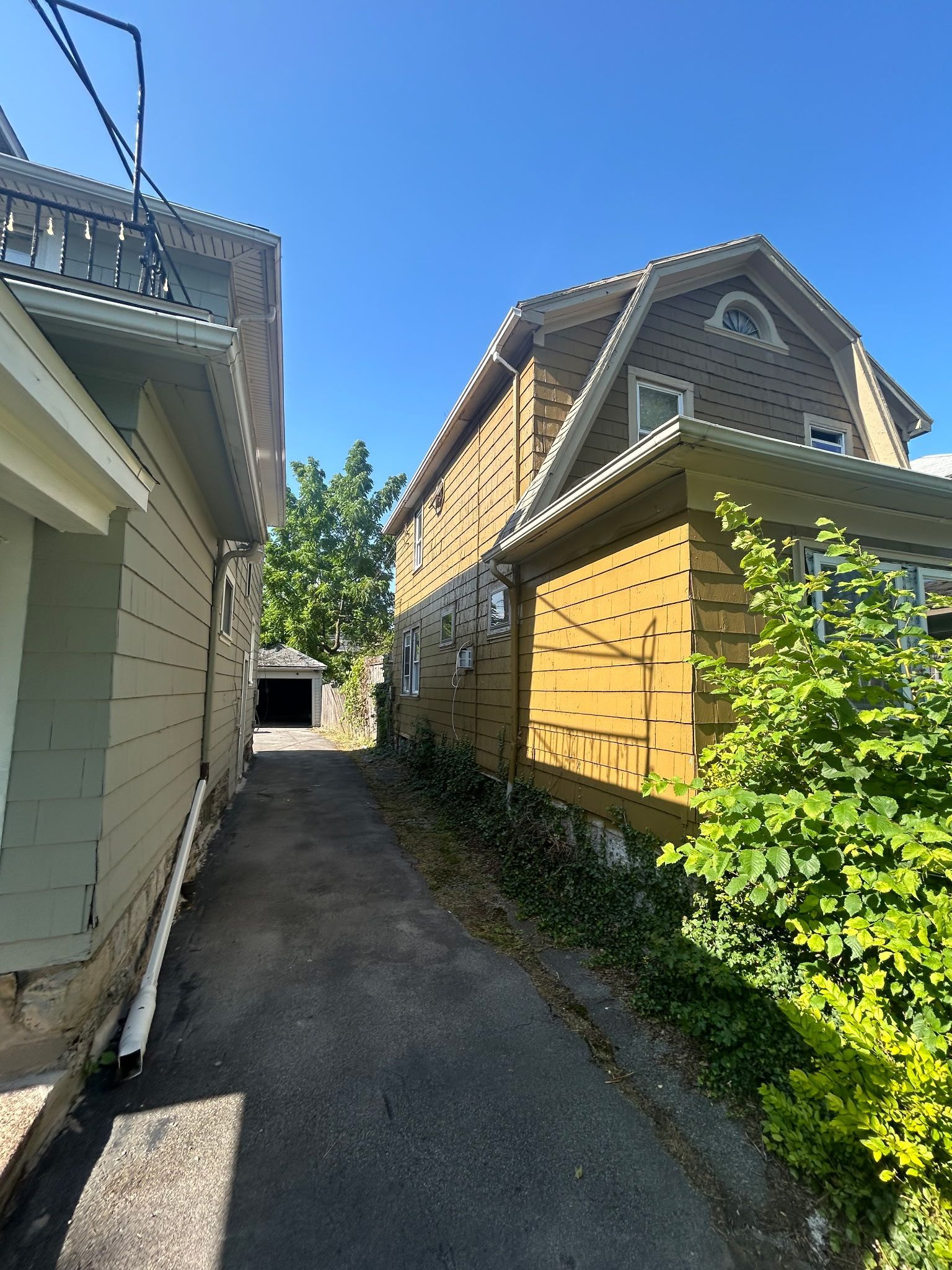 Narrow walkway between two houses, with beige siding, a yellow house, and blue sky overhead.