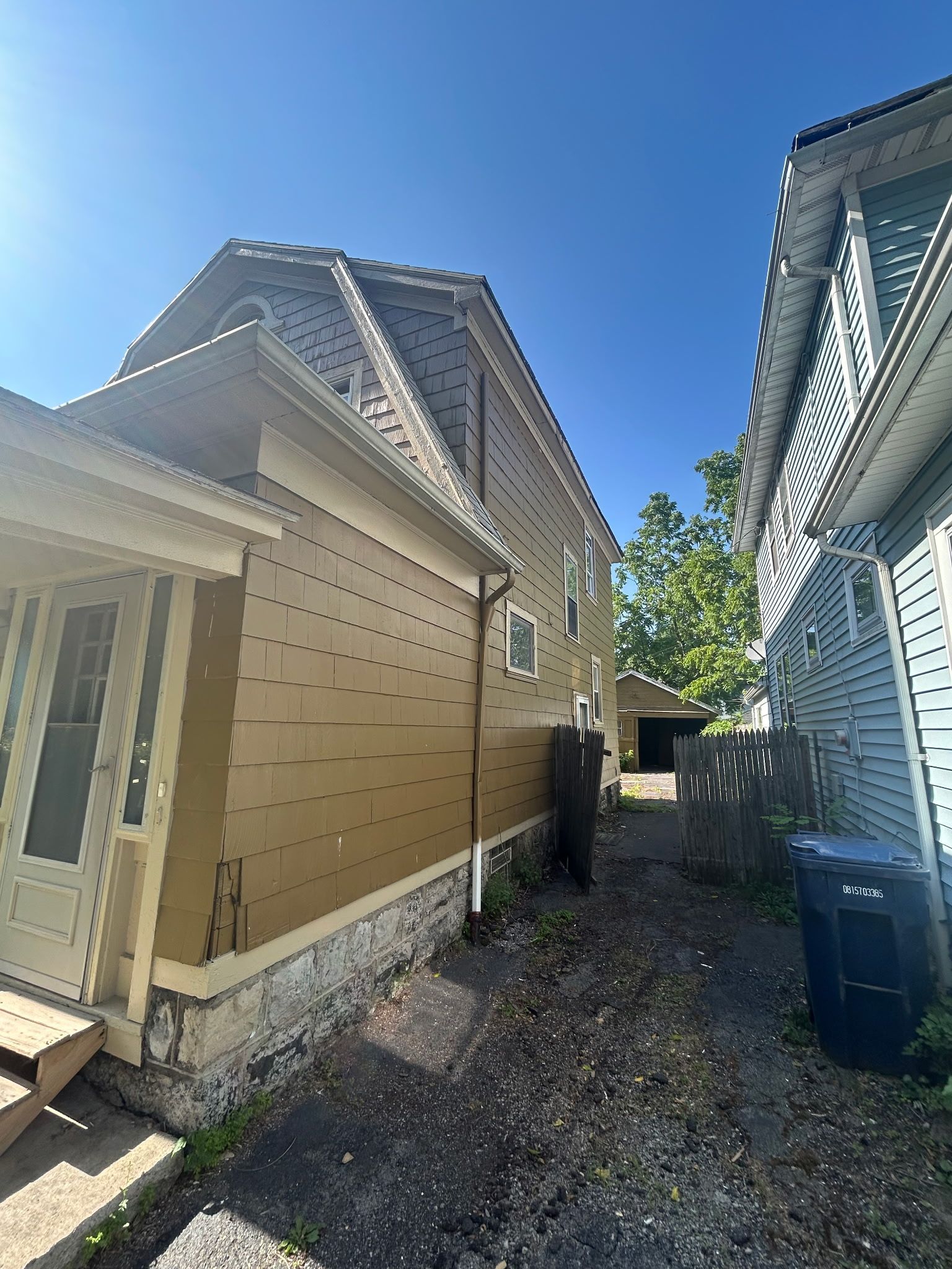 Narrow side yard between beige and blue houses with gravel ground and bright blue sky
