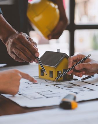 A person is pointing at a model house on a table