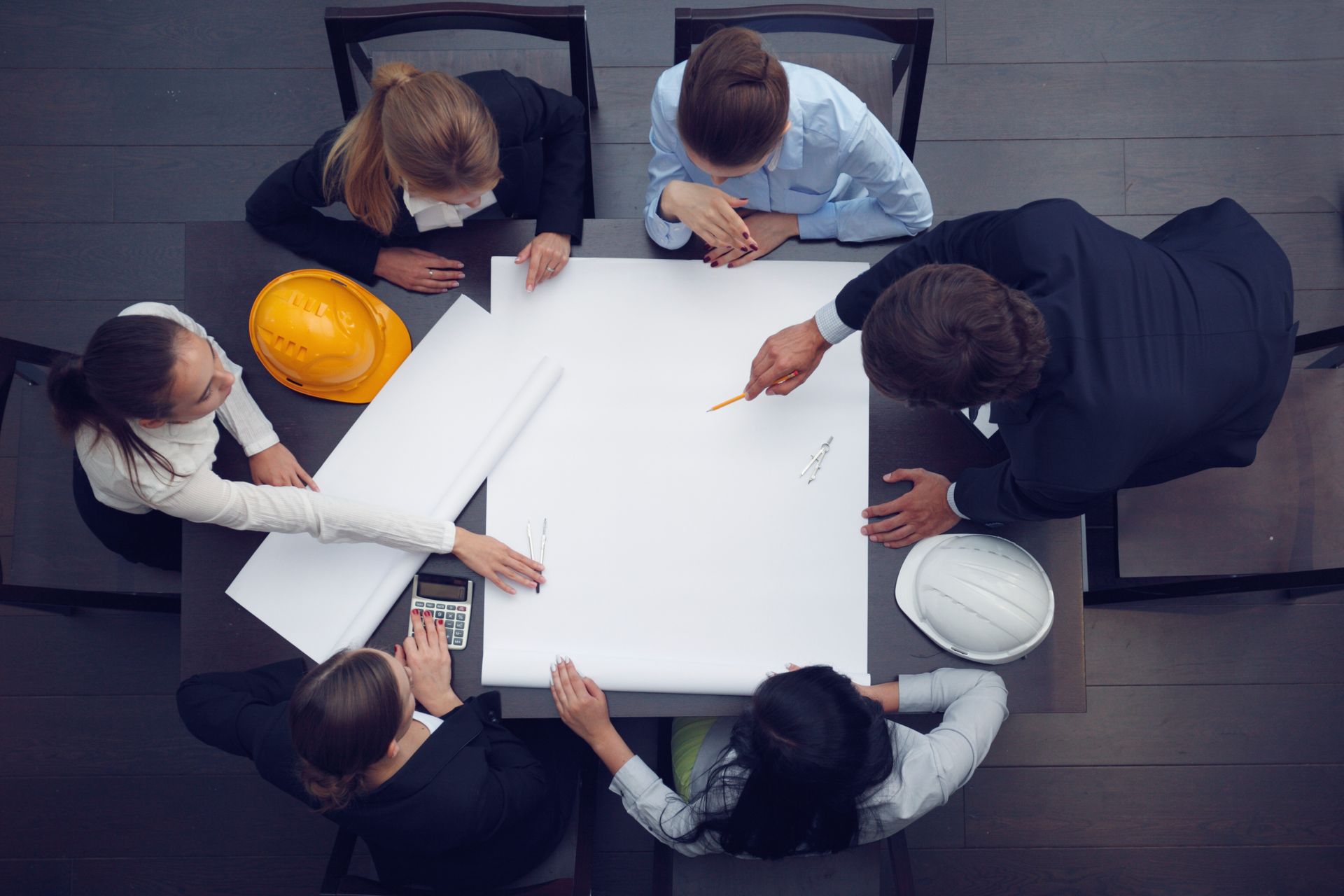 A group of people are sitting around a table looking at a blueprint.