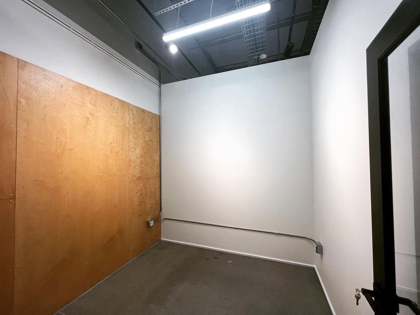 Empty room with white walls, wooden door, exposed ceiling, and gray carpeted floor.