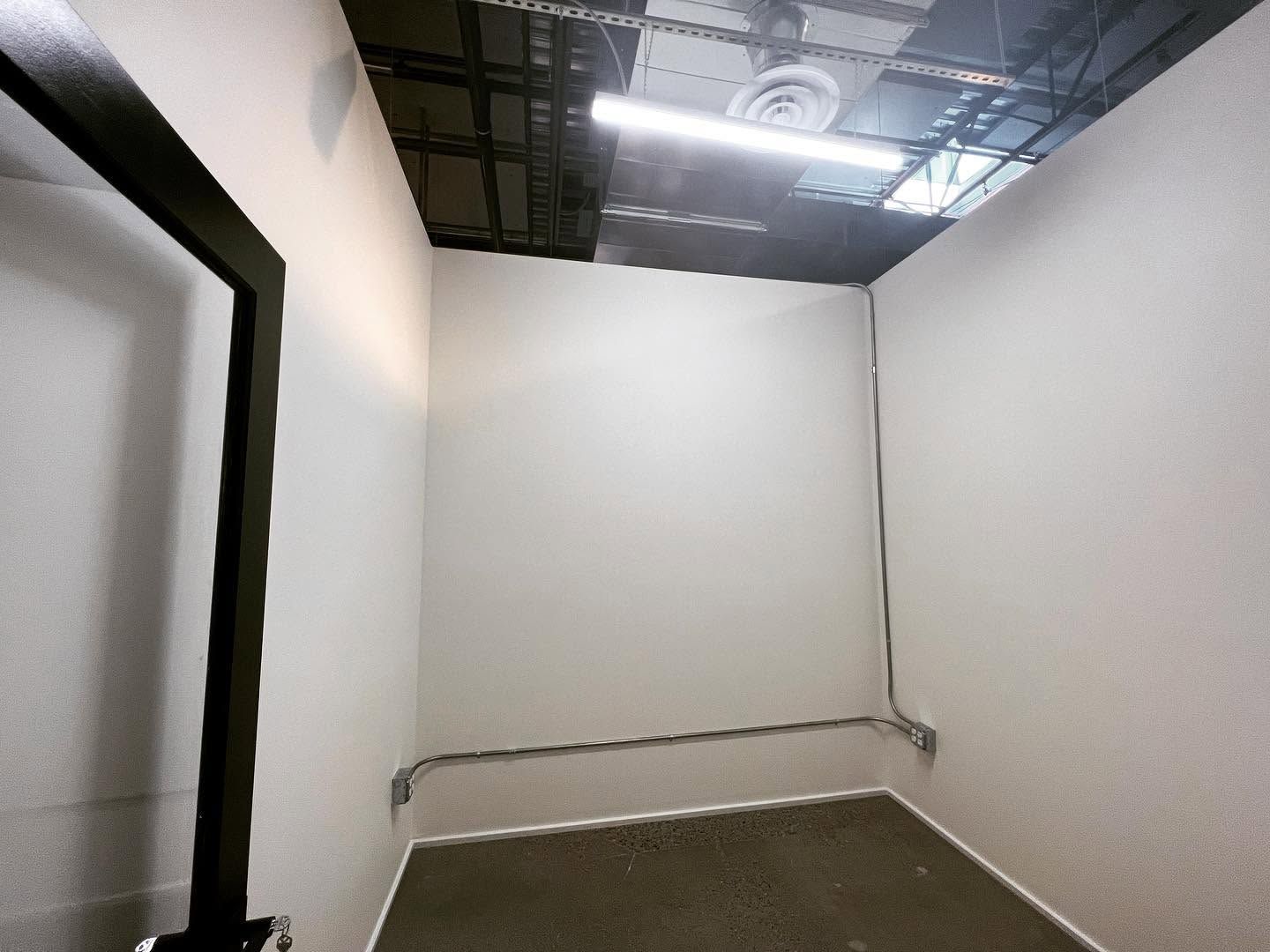 Empty industrial room with white walls, exposed ceiling, and gray concrete floor