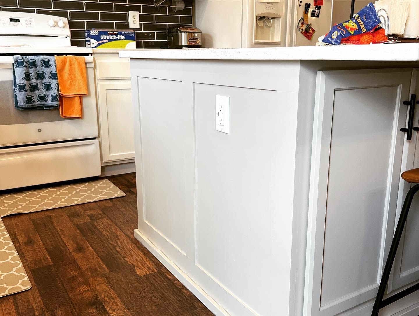Kitchen with white island, dark wood floor, beige cabinets, and oven near a patterned rug