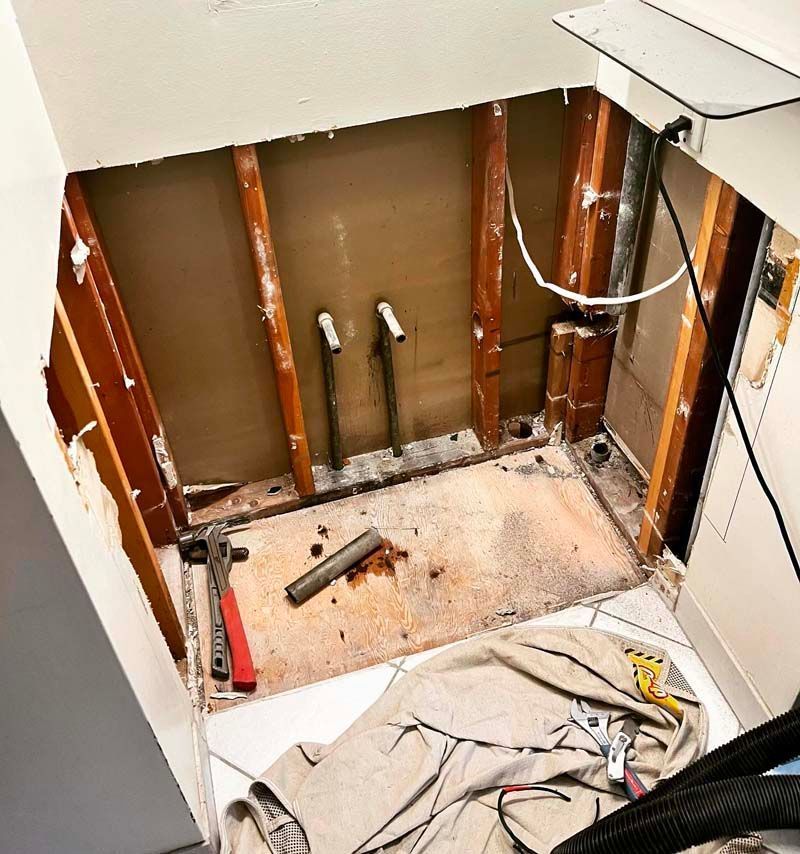 Bathroom under renovation with exposed wall studs, removed fixtures, and construction debris on the floor