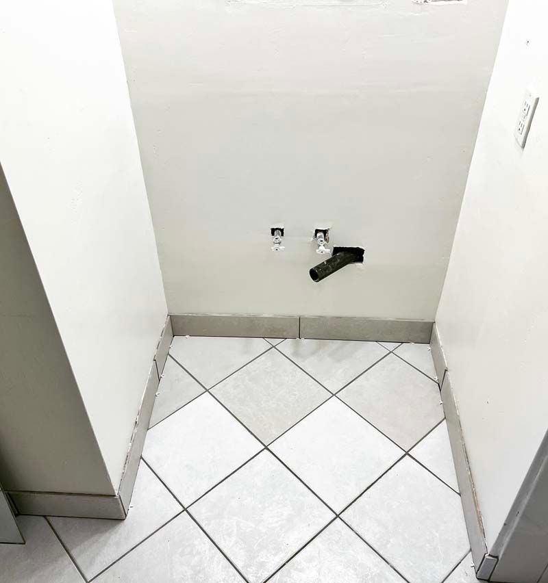 Small tiled alcove with wall plumbing connections and a black pipe or fixture near the floor.