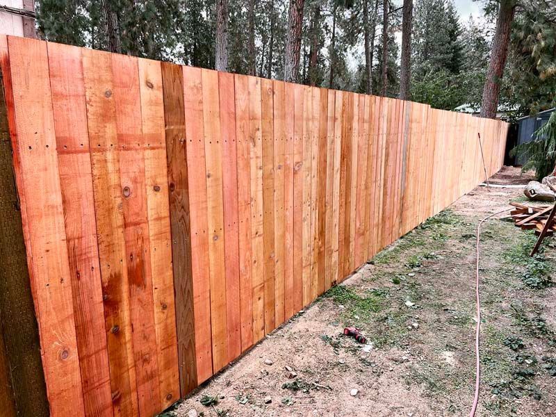 Long wooden fence with warm stained boards along a wooded yard
