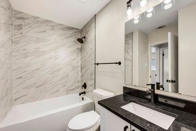 Modern bathroom with marble walls, white tub, toilet, and dark vanity with large mirror