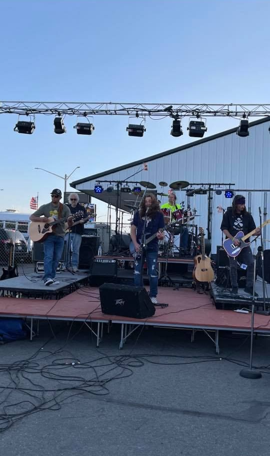 A band performs on a stage outside. Instruments include guitars and drums.