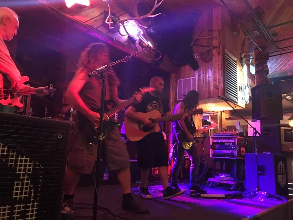 Band performing live on a small stage under pink and purple lights