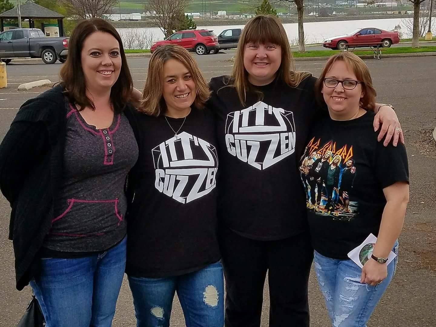 Four people in a parking lot, posing for a photo. Three are wearing matching