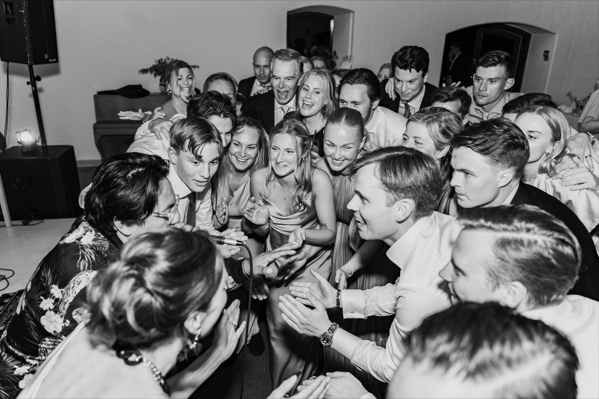 Crowded room of people gathered closely, smiling and talking around a central table or activity