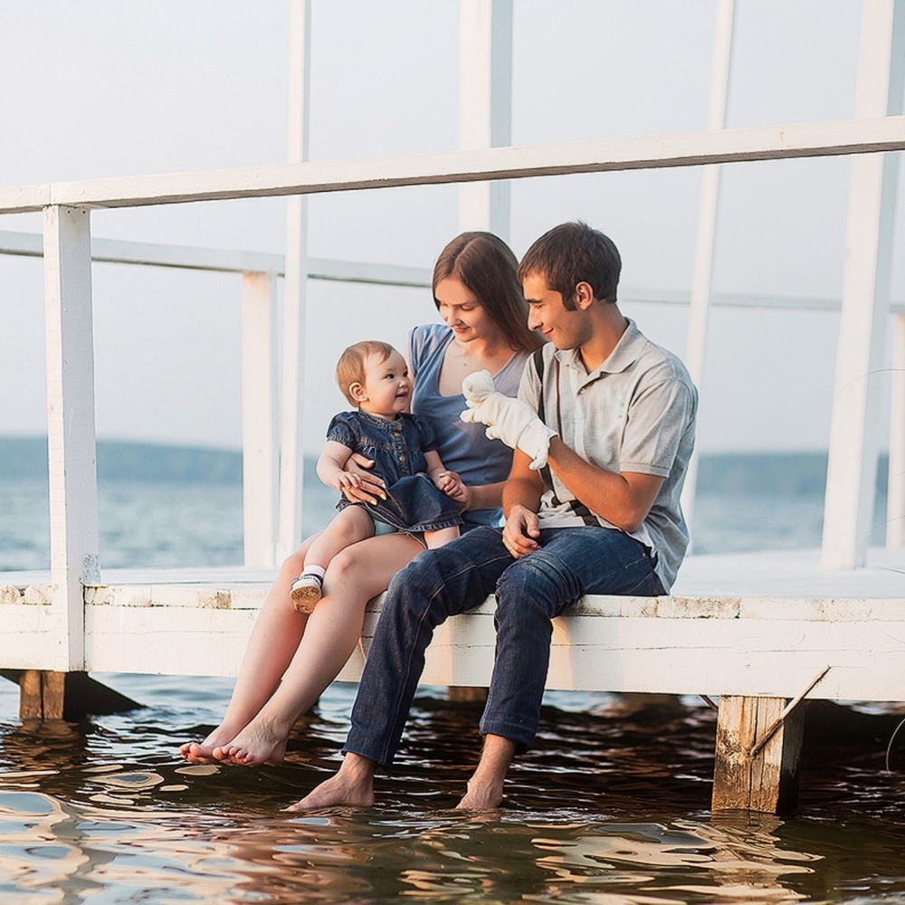 A man and woman are sitting on a dock holding a baby