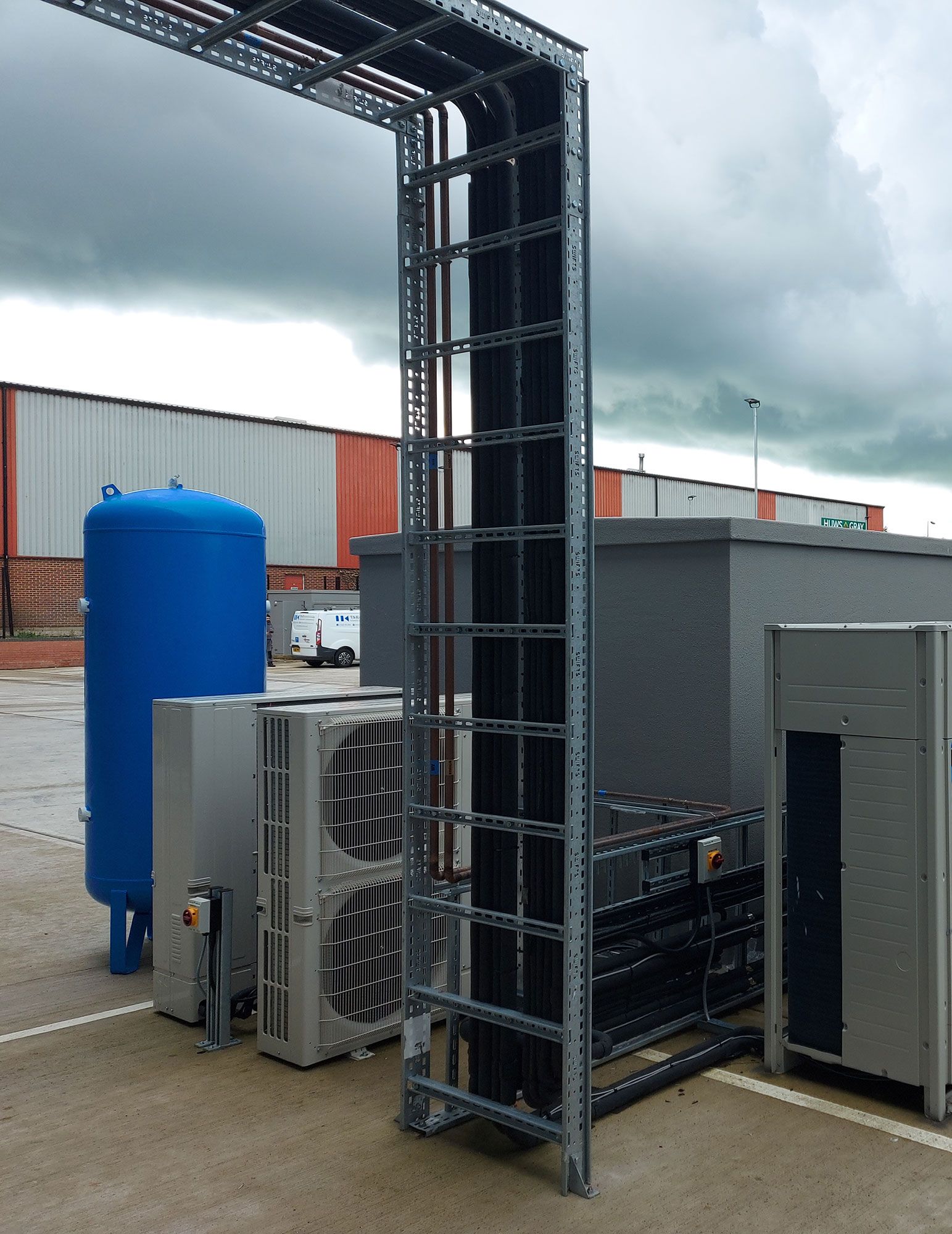 Industrial rooftop equipment with blue tank, metal ductwork, and gray enclosure under cloudy sky