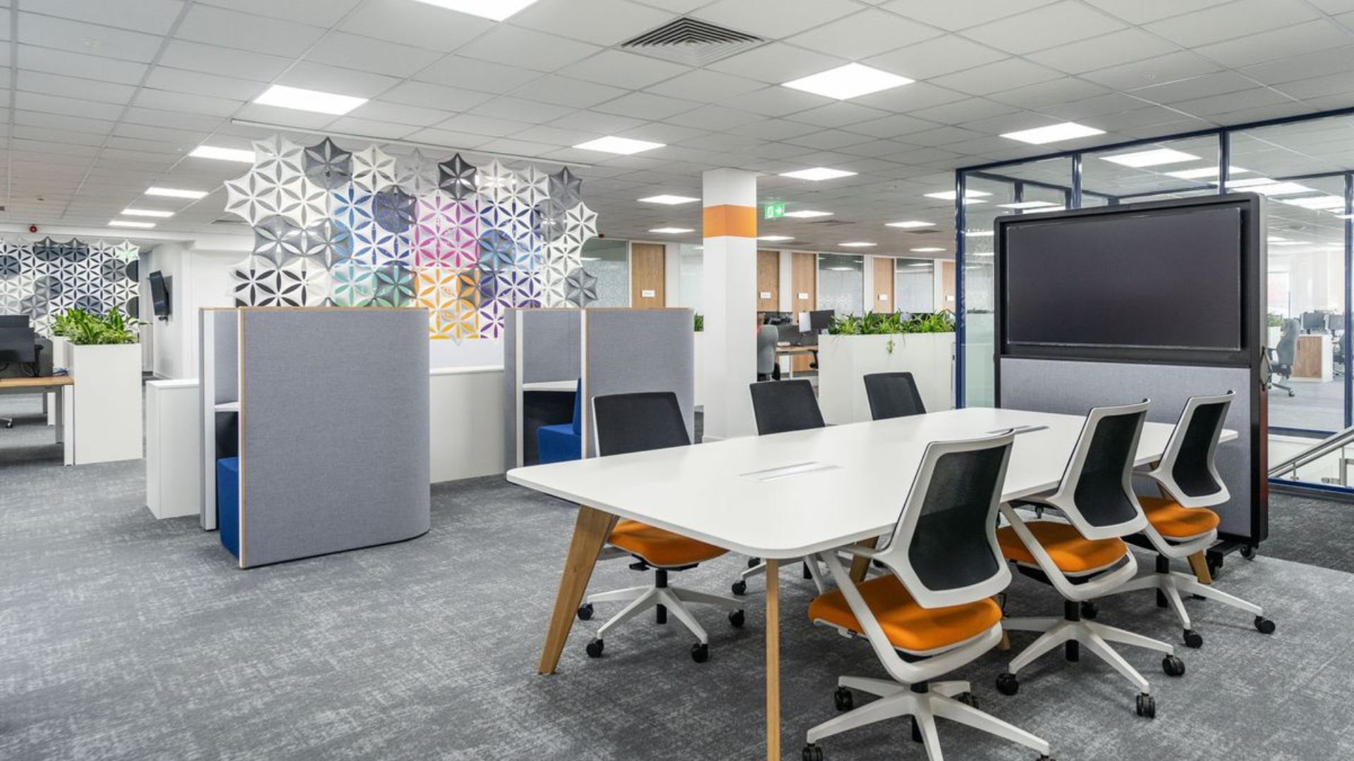 Modern office with desks, chairs, partitions, and a large presentation screen