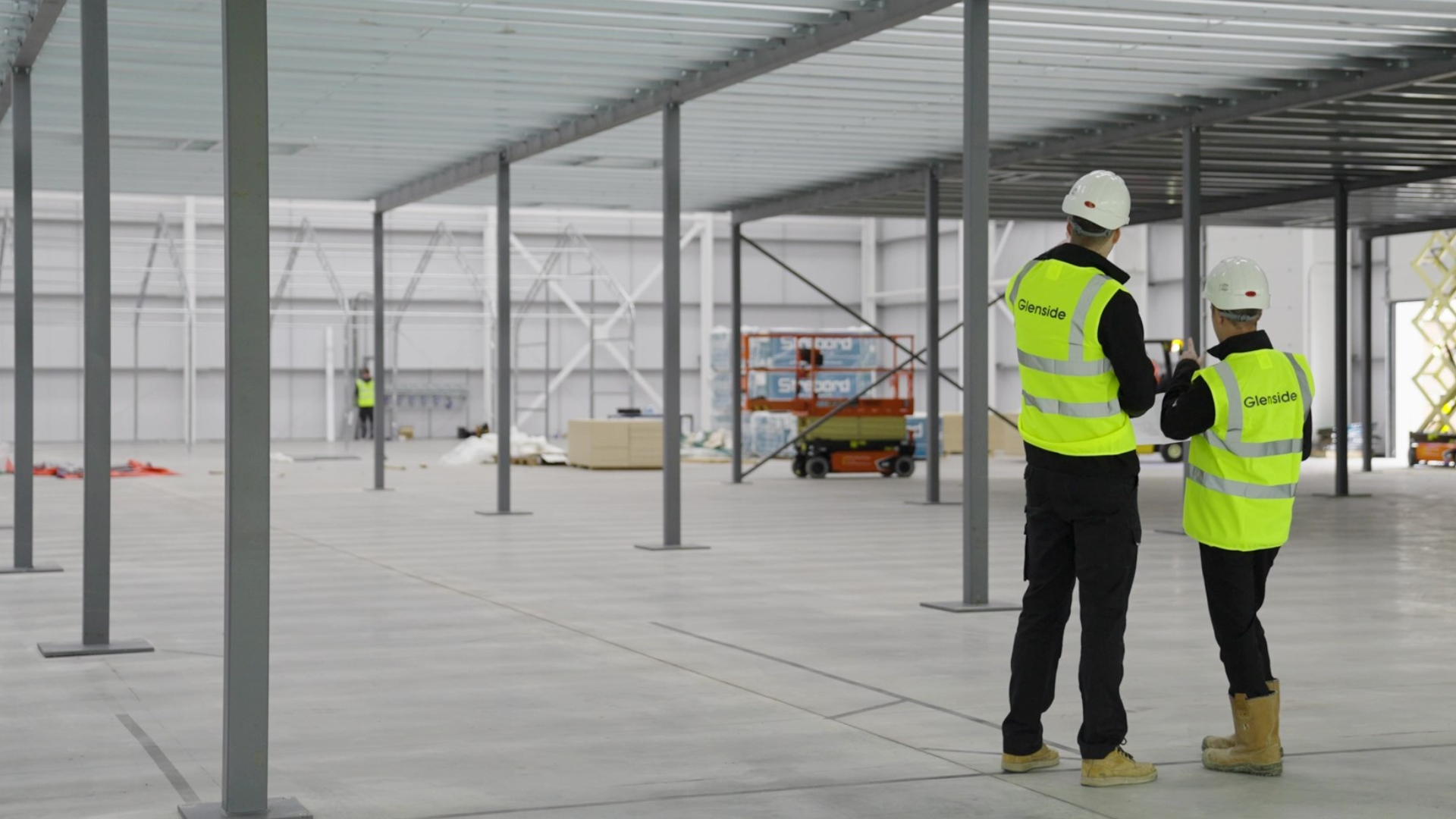Two workers in high-visibility vests inspecting a construction site interior under steel framing