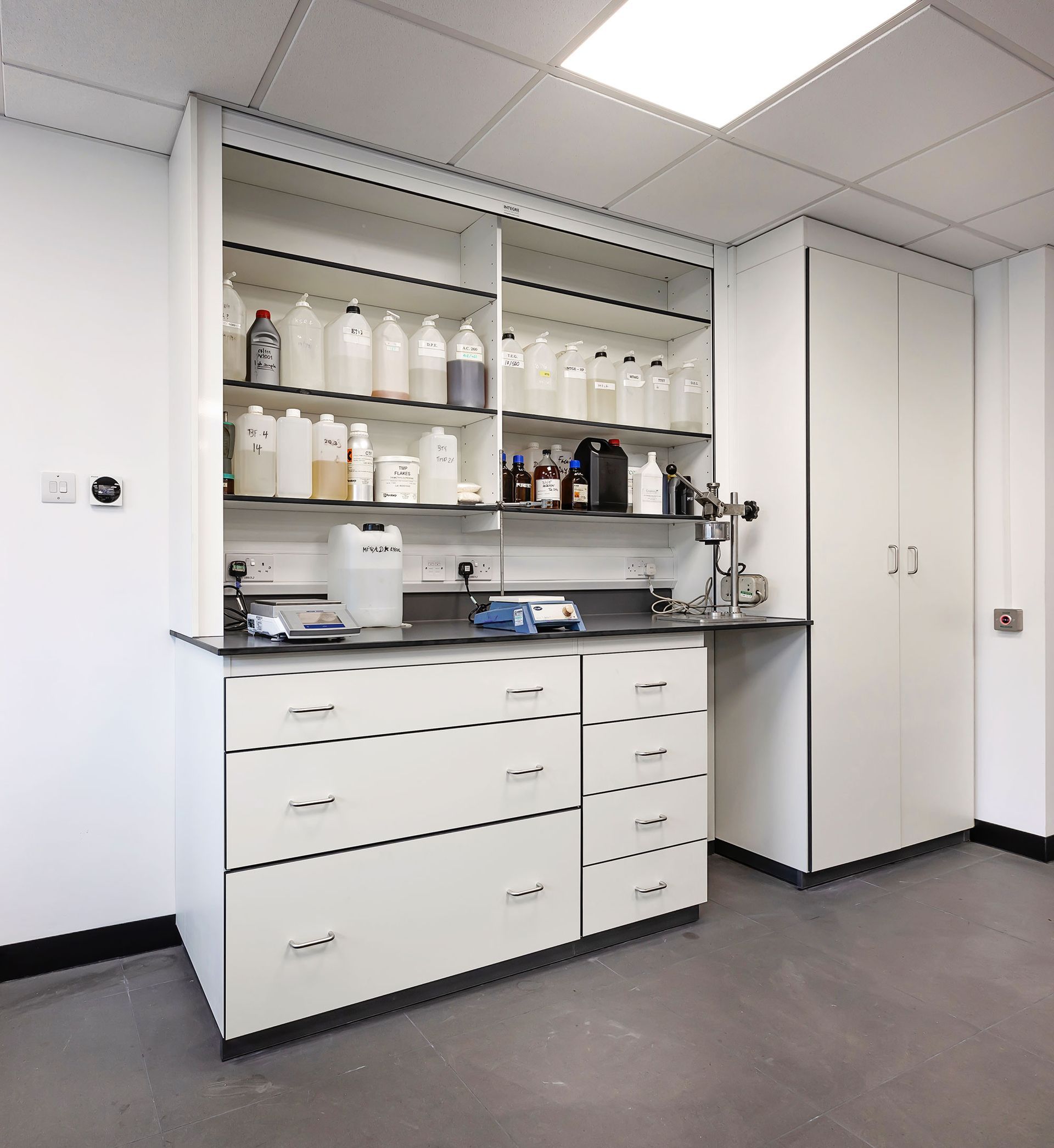 Laboratory bench with cabinets, shelves of bottles, and stainless steel sink in a clean room