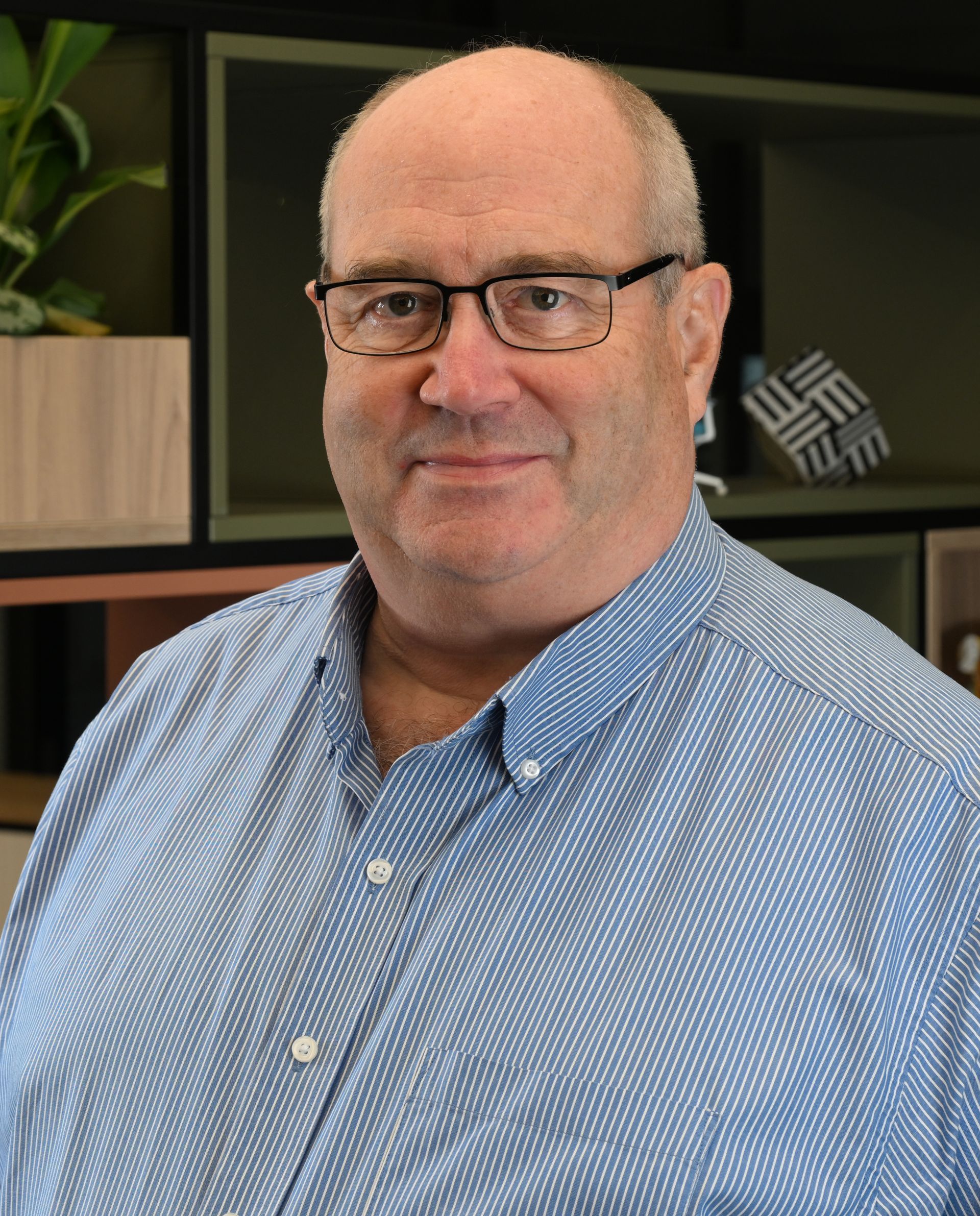 Man seated at a desk in a striped shirt, facing the camera in an office.