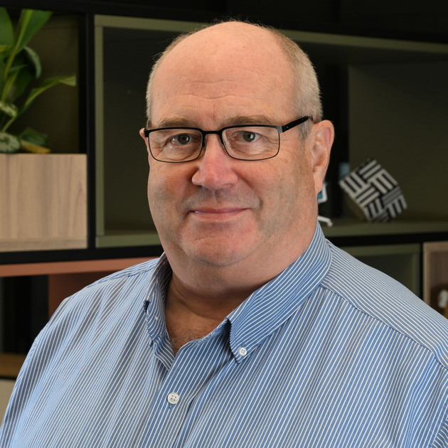 Man seated at a desk in a striped shirt, facing the camera in an office setting.