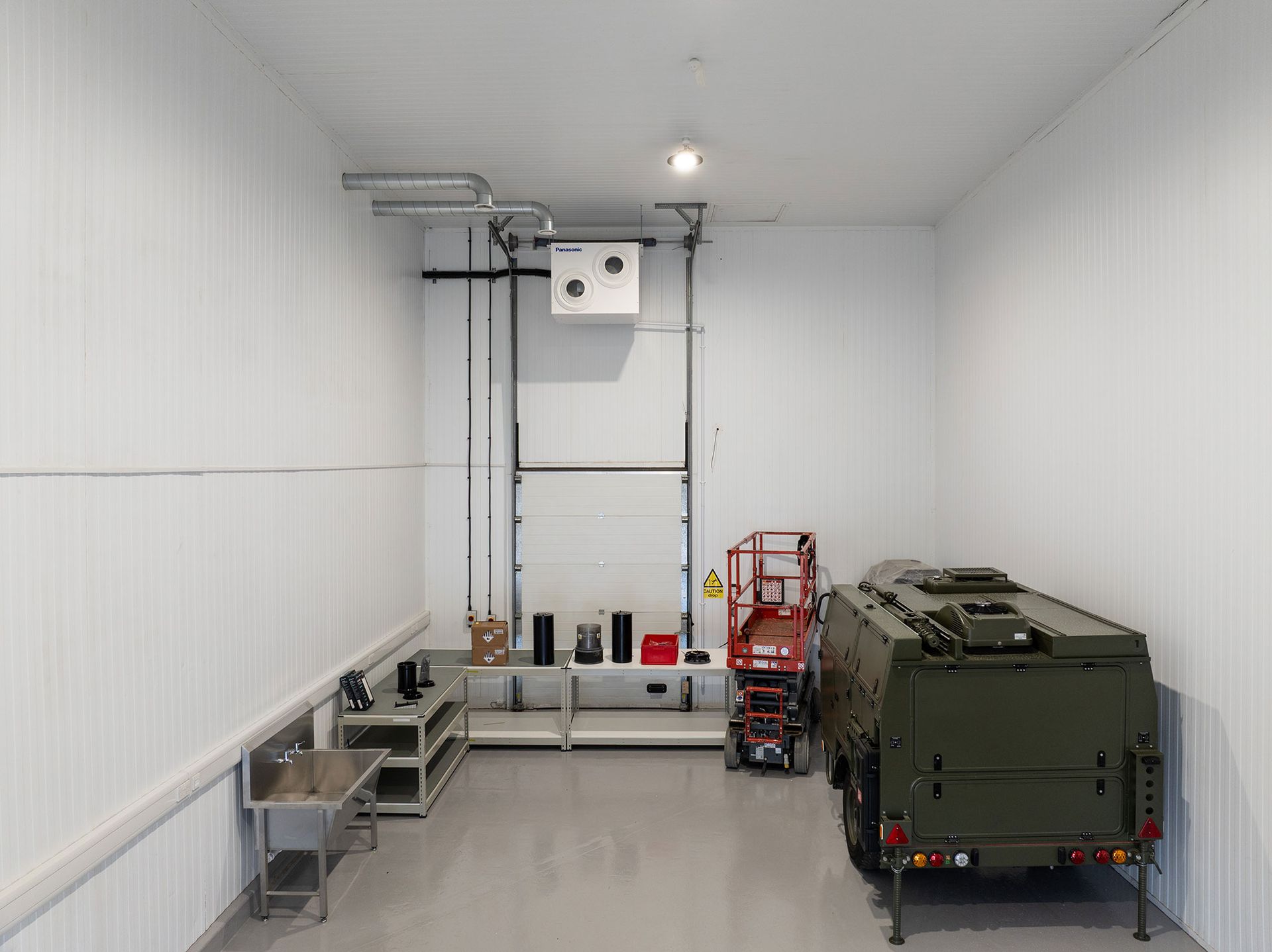 Empty white utility room with equipment, shelves, and a green machine along the right wall