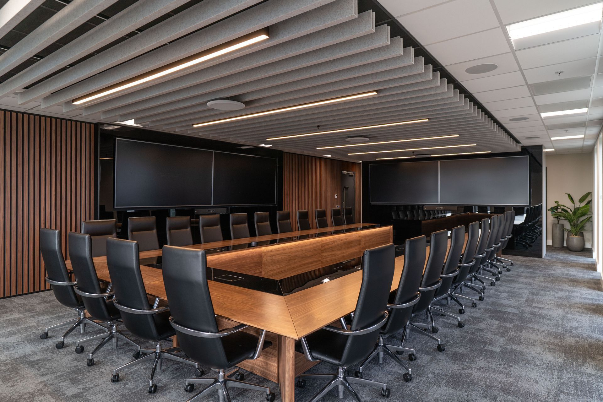 Modern conference room with long wooden table, black chairs, and large wall-mounted screens