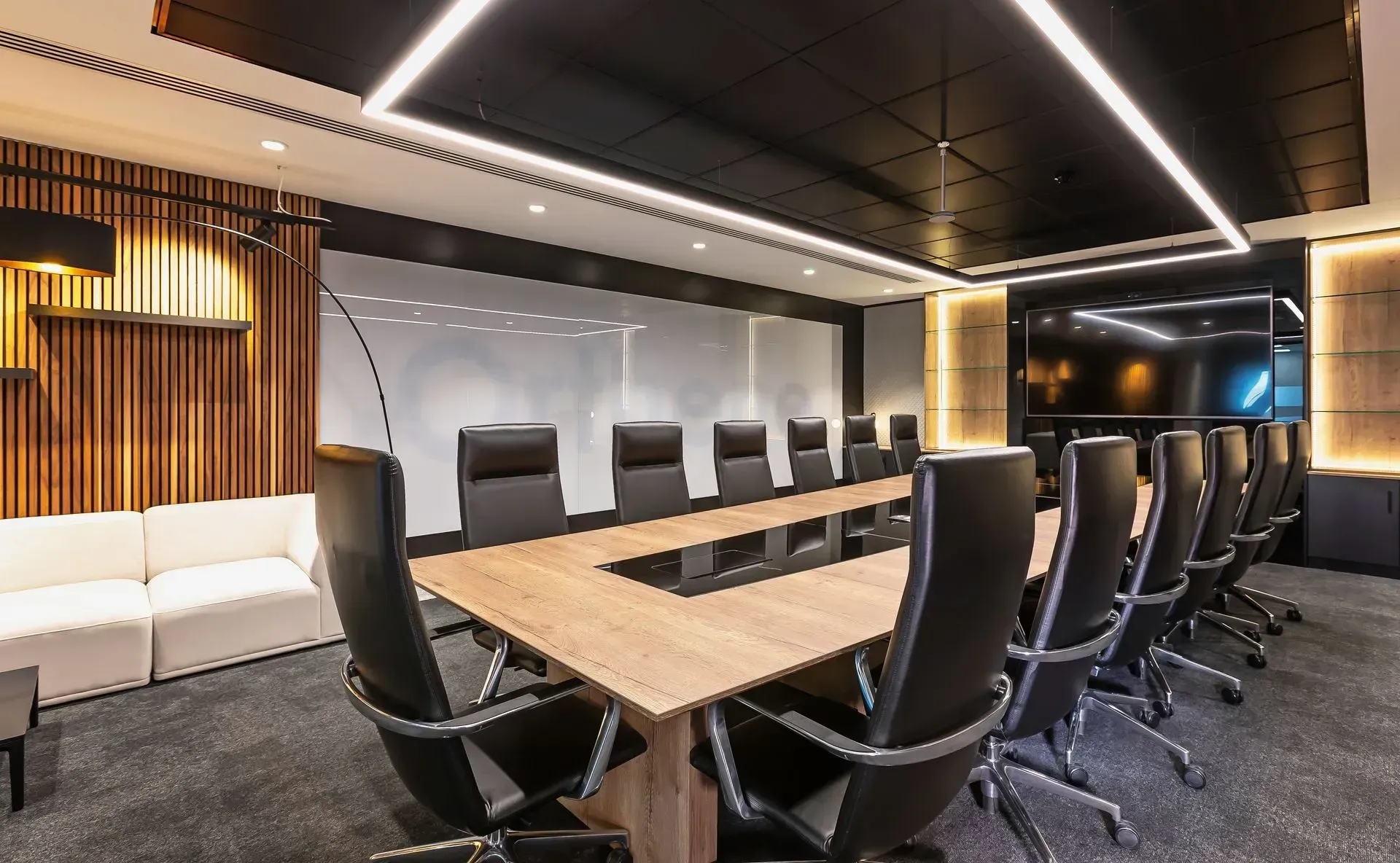 Modern conference room with long wooden table, black chairs, and wood-accent walls and lighting
