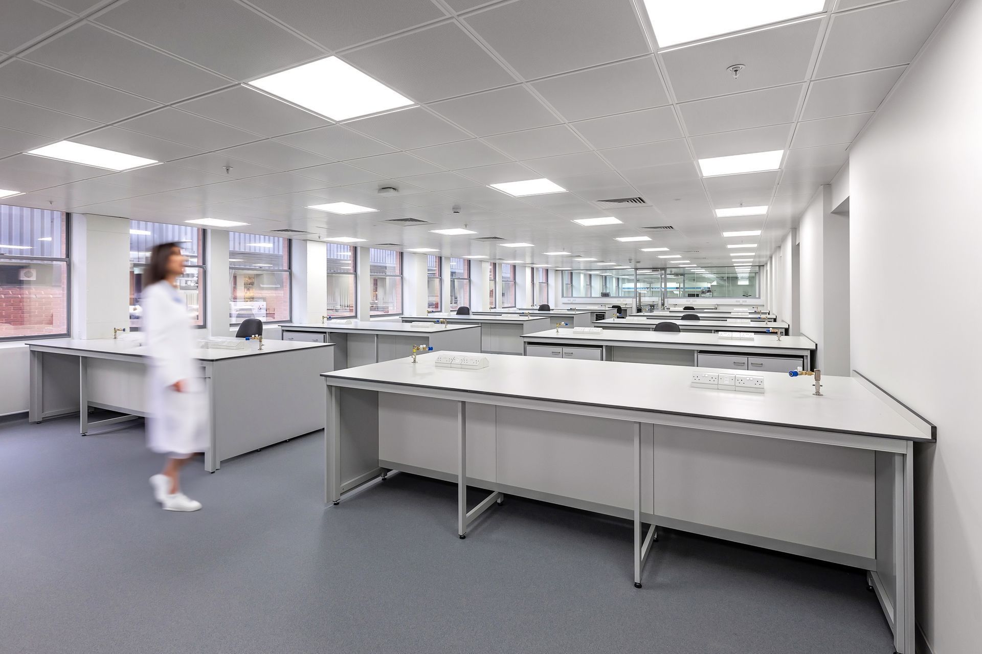 Bright laboratory with white counters and a person in a lab coat walking inside