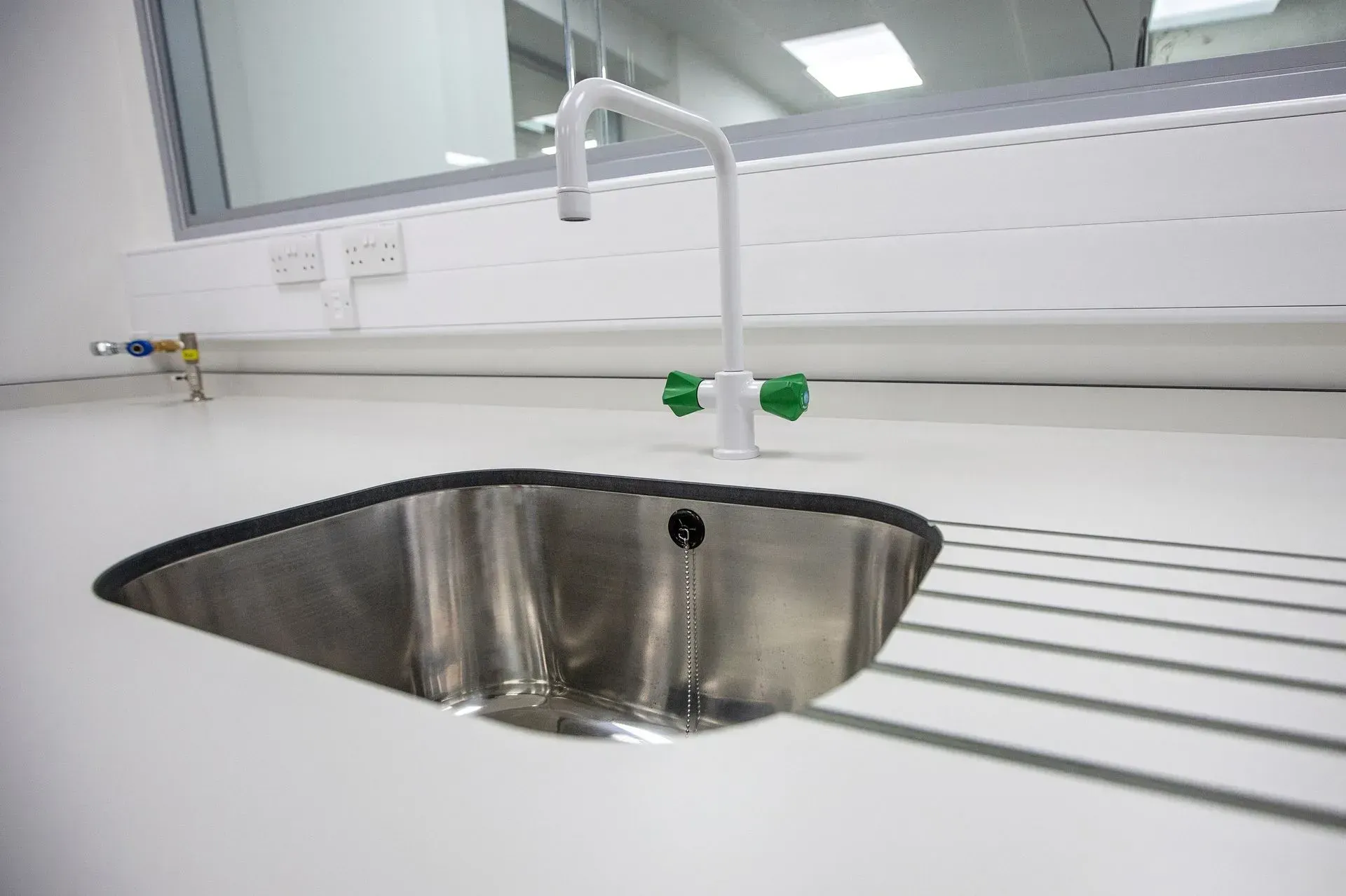 Modern kitchen sink with stainless steel basin, white countertop, and window above the faucet
