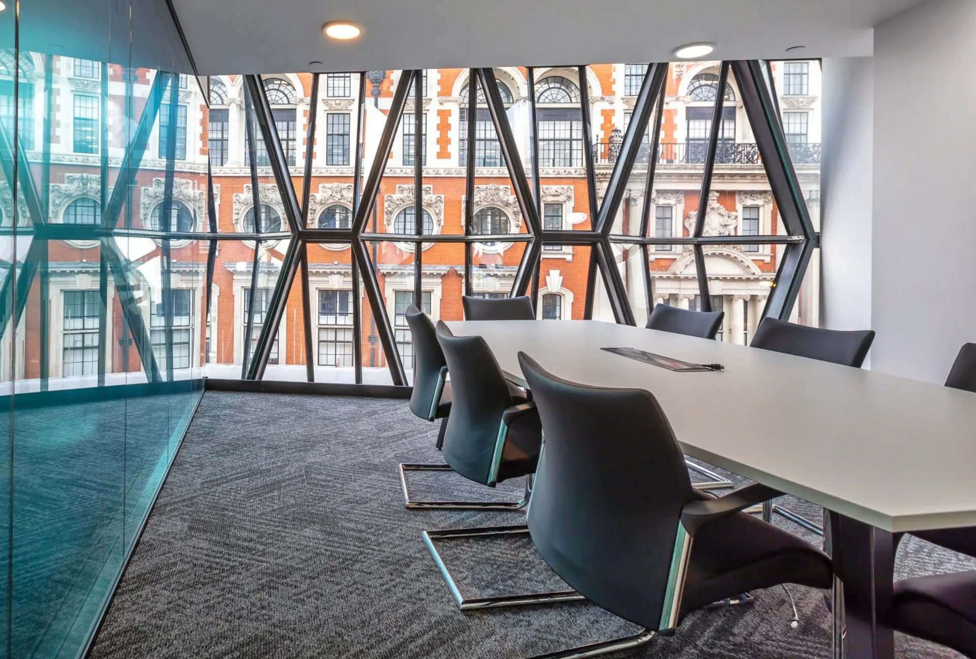 Modern conference room with long white table, black chairs, and floor-to-ceiling windows overlooking buildings