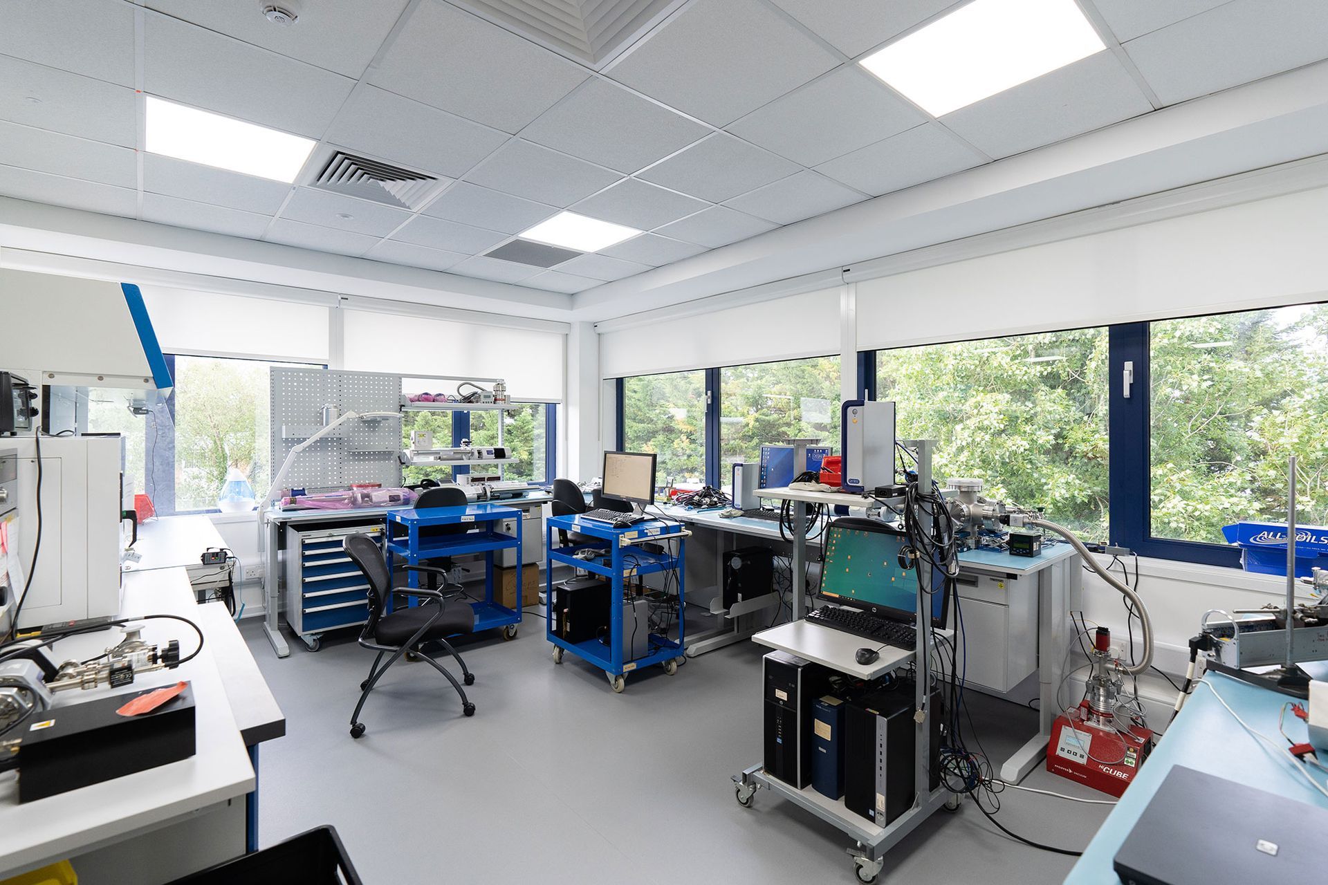 Bright electronics lab with workbenches, equipment racks, and large windows overlooking trees