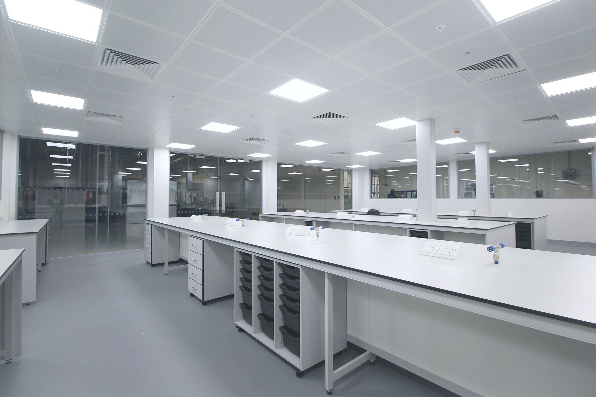Empty modern laboratory with white workbenches, gray floor, and glass-walled rooms in the background