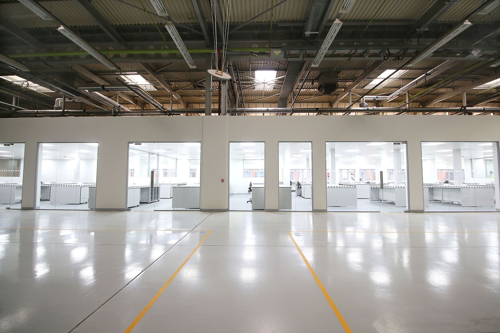 Empty industrial warehouse interior with glossy white floor, open bays, and exposed ceiling beams