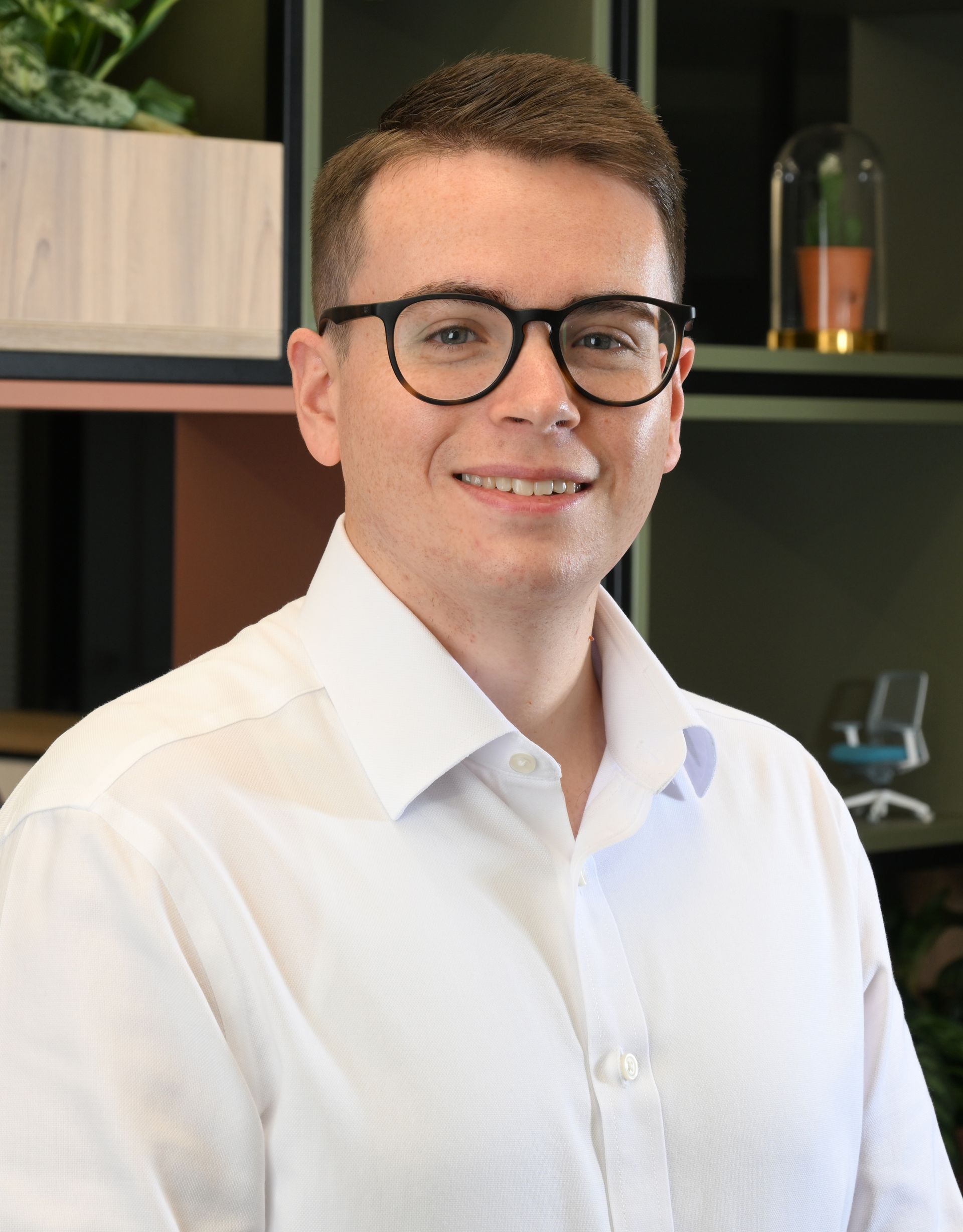 Portrait of a person with glasses and a dark shirt, standing against a light gray background
