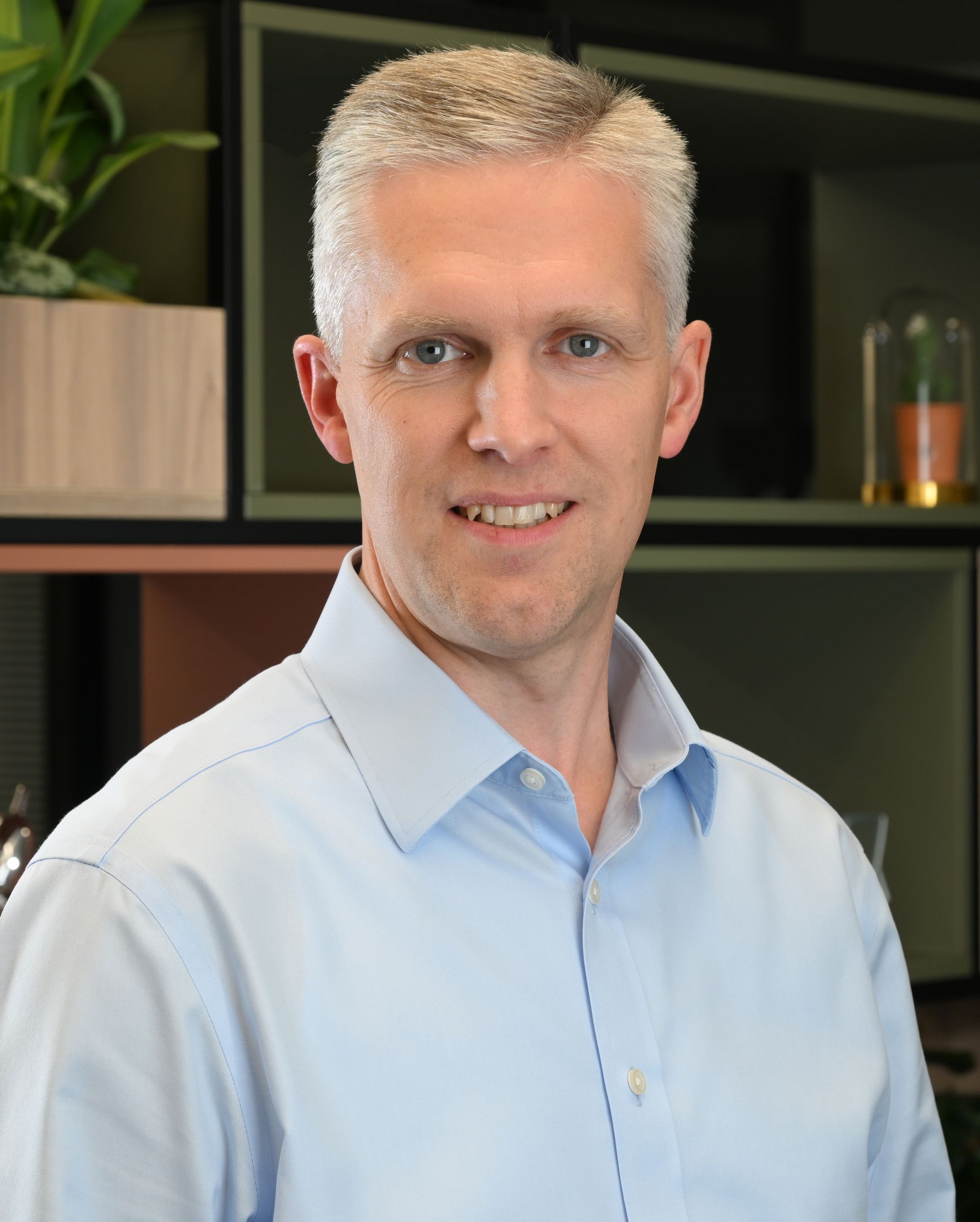 Man in a white shirt standing indoors with a slight smile