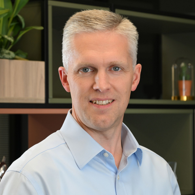 Portrait of a smiling man in a white shirt standing indoors against a modern office background