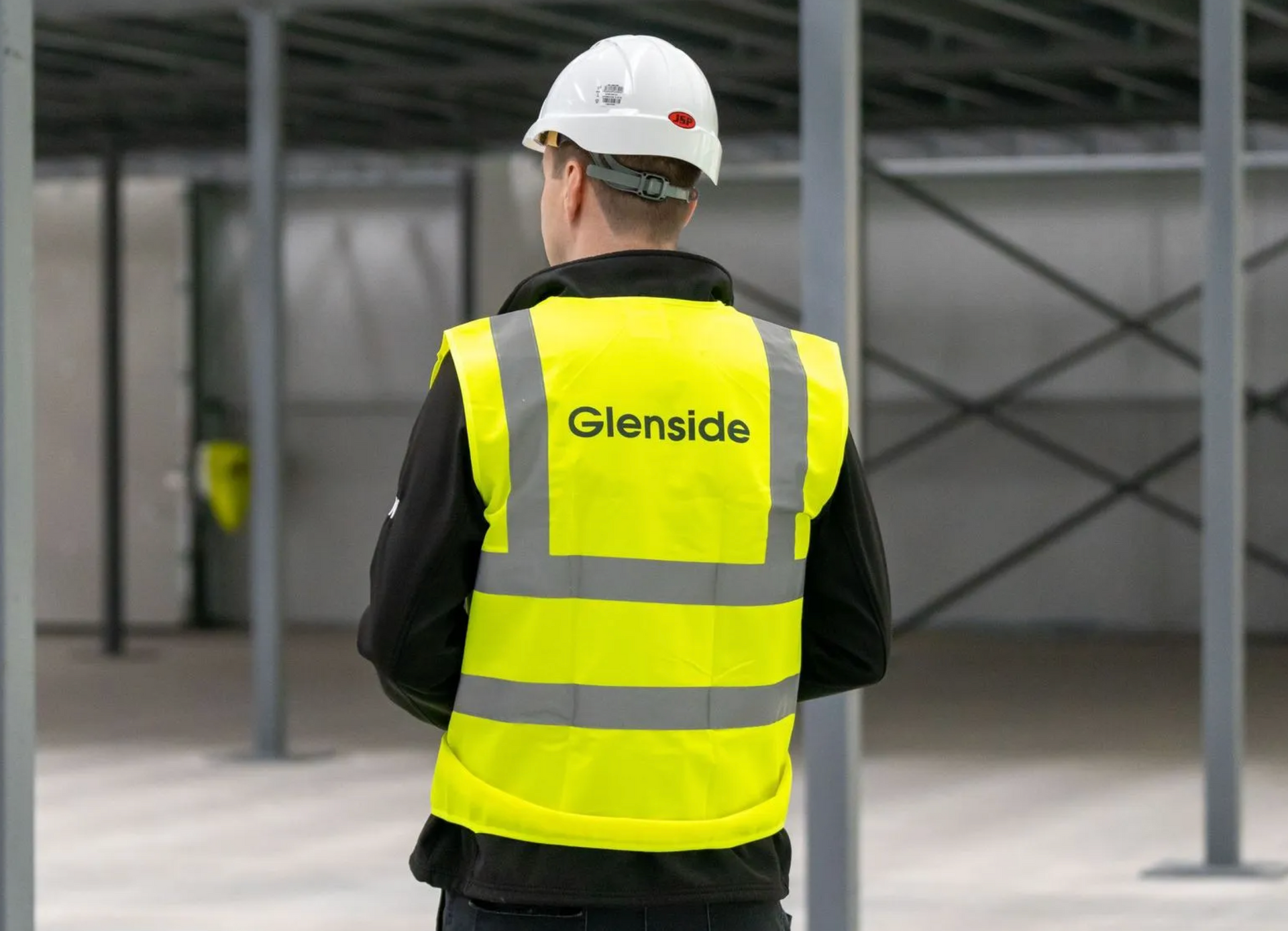 Worker in white hard hat and neon yellow vest standing in a construction site with steel beams.