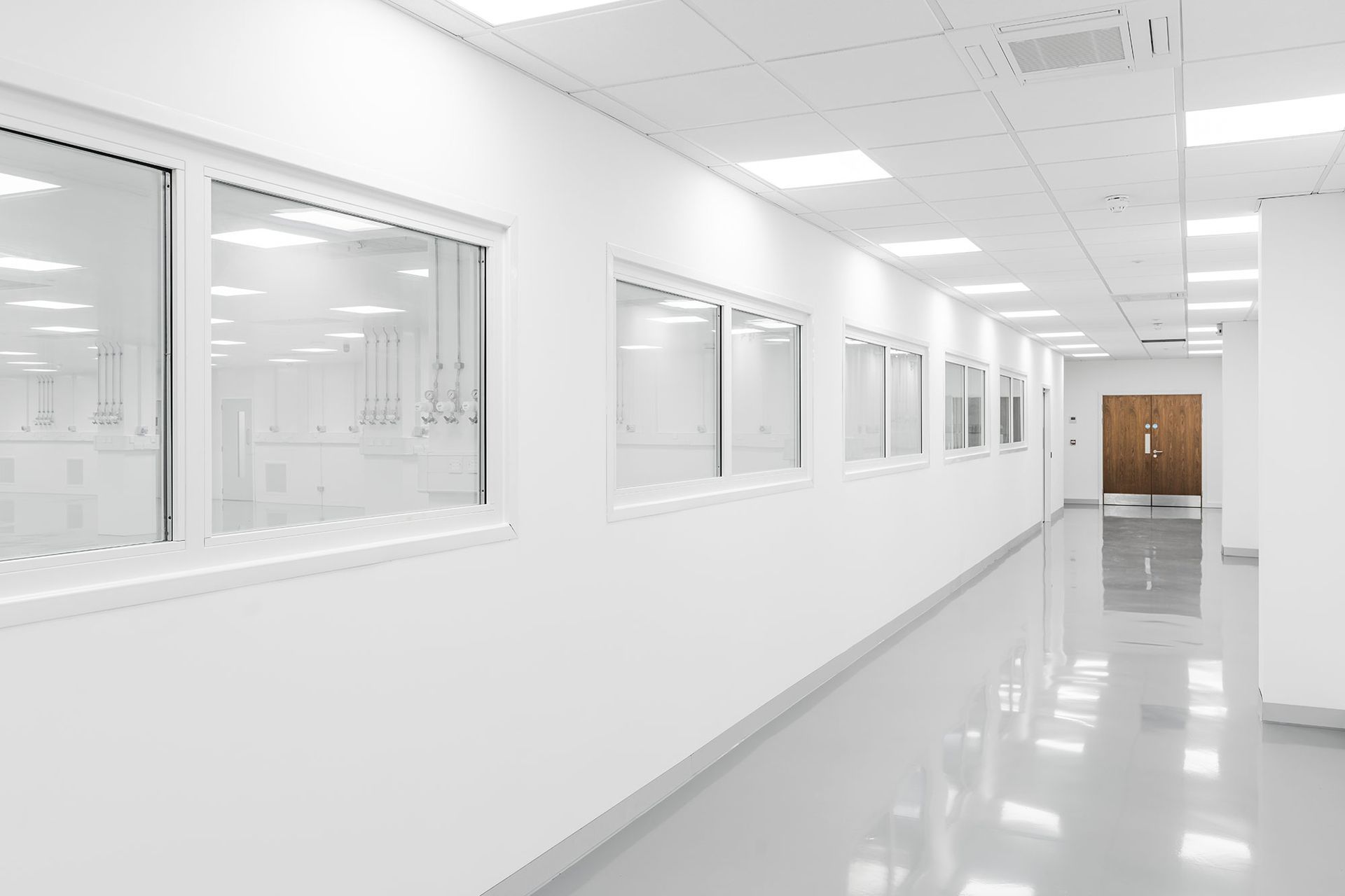 Bright white hospital corridor with windows, glossy floor, and double doors at the end