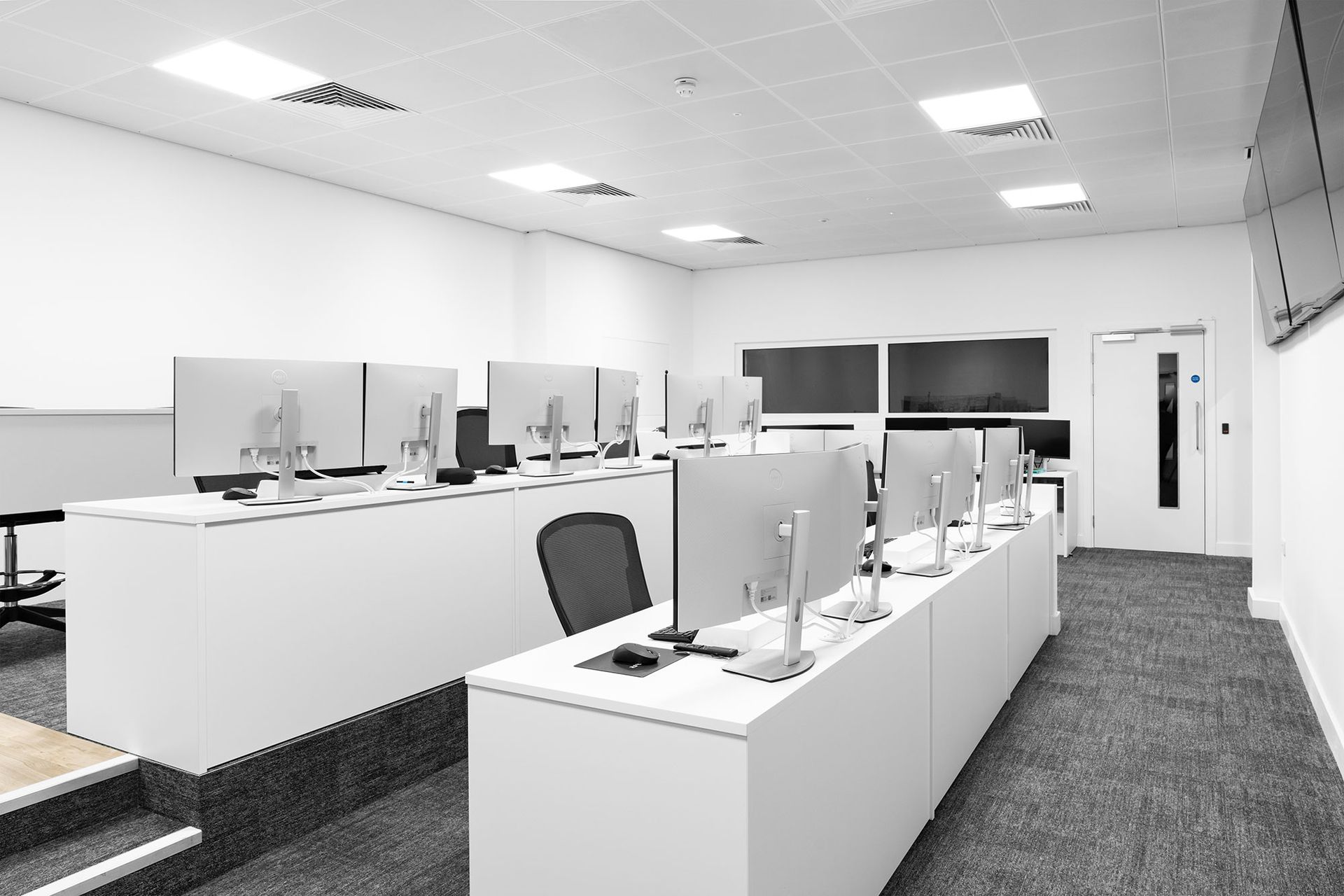 Empty modern office with white desks, computer monitors, and gray carpet under bright ceiling lights