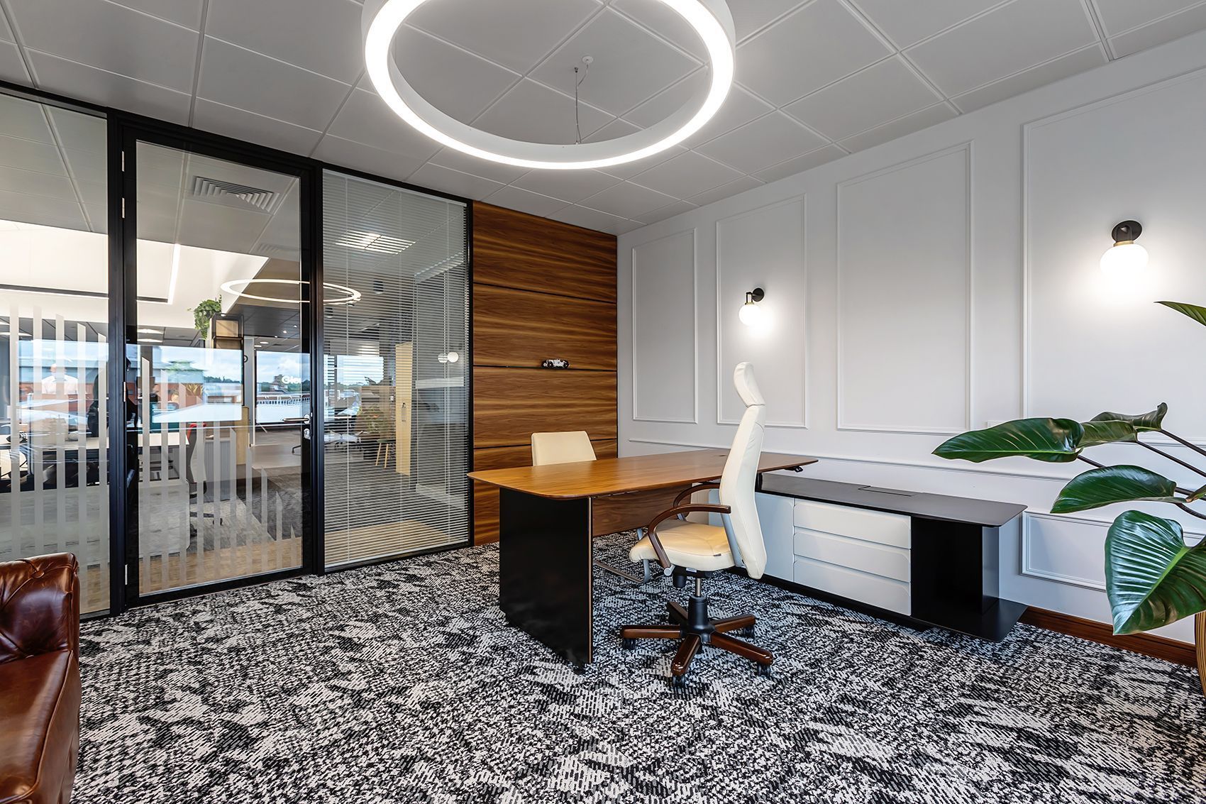 Modern office workspace with desks, shelves, plants, and two people meeting in a bright open area
