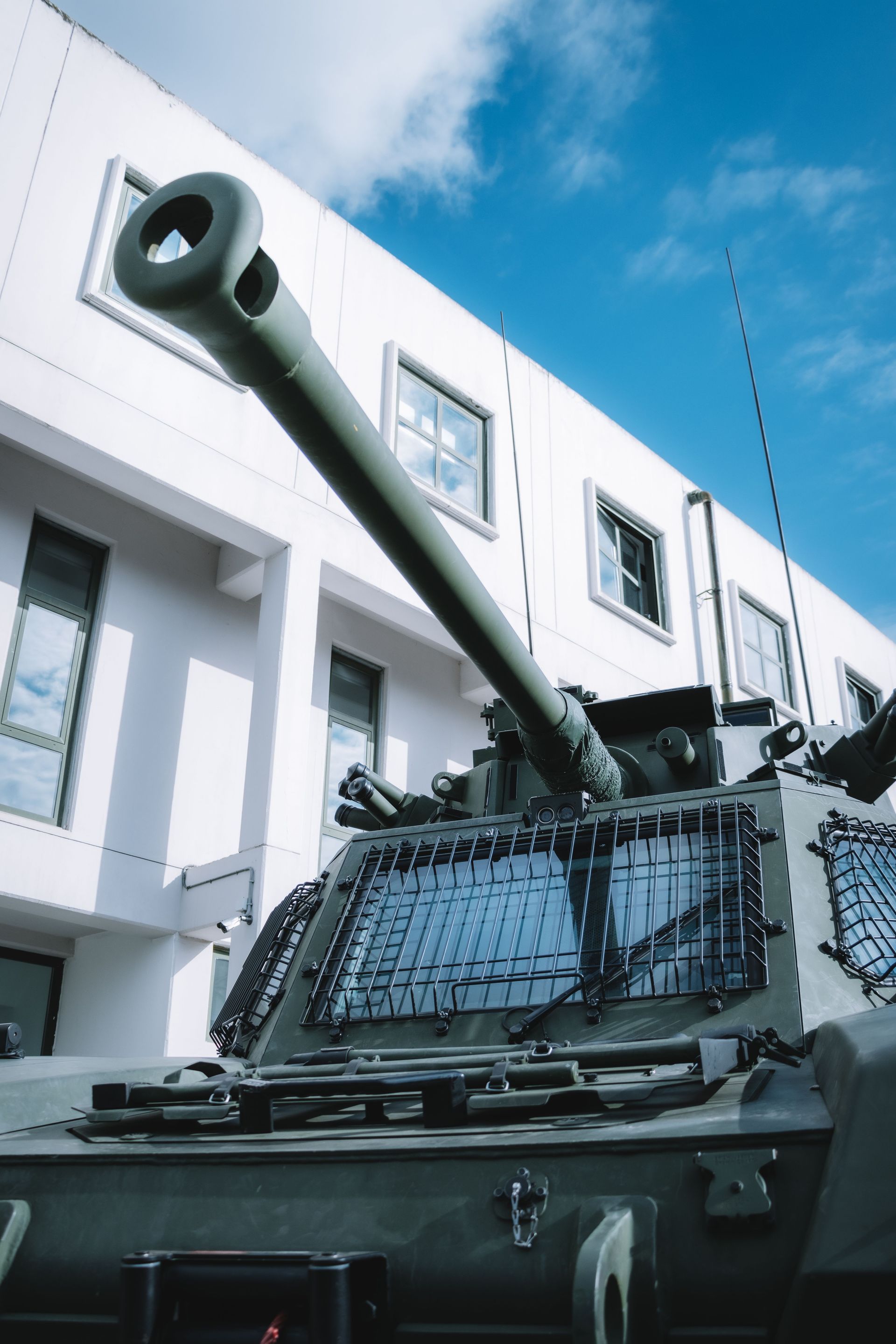 Tank turret pointing at a white building under a blue sky