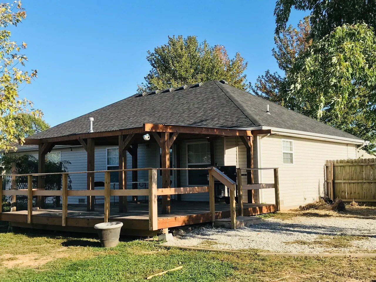A small house with a porch and a fence in front of it.