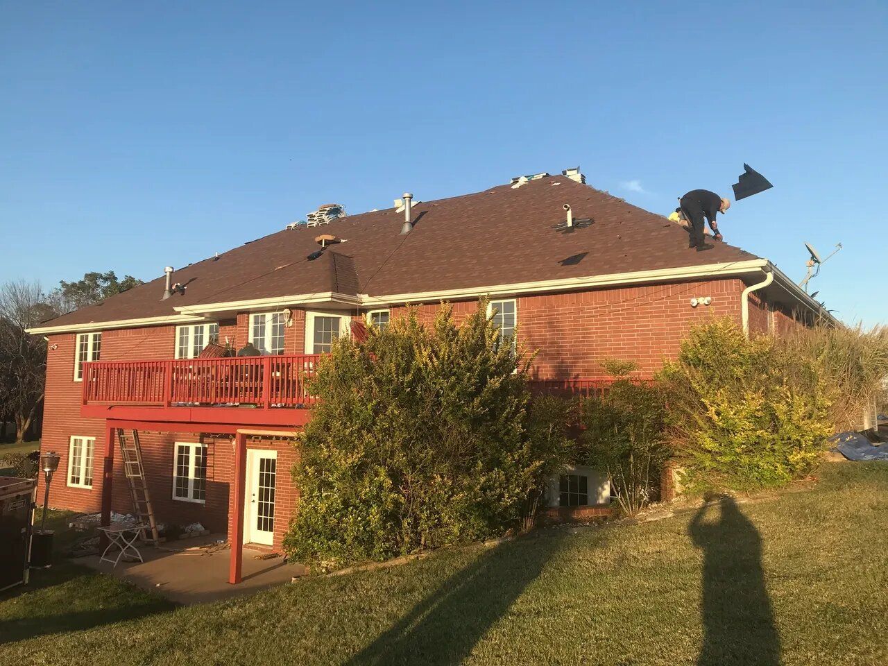 A man is working on the roof of a large brick house.