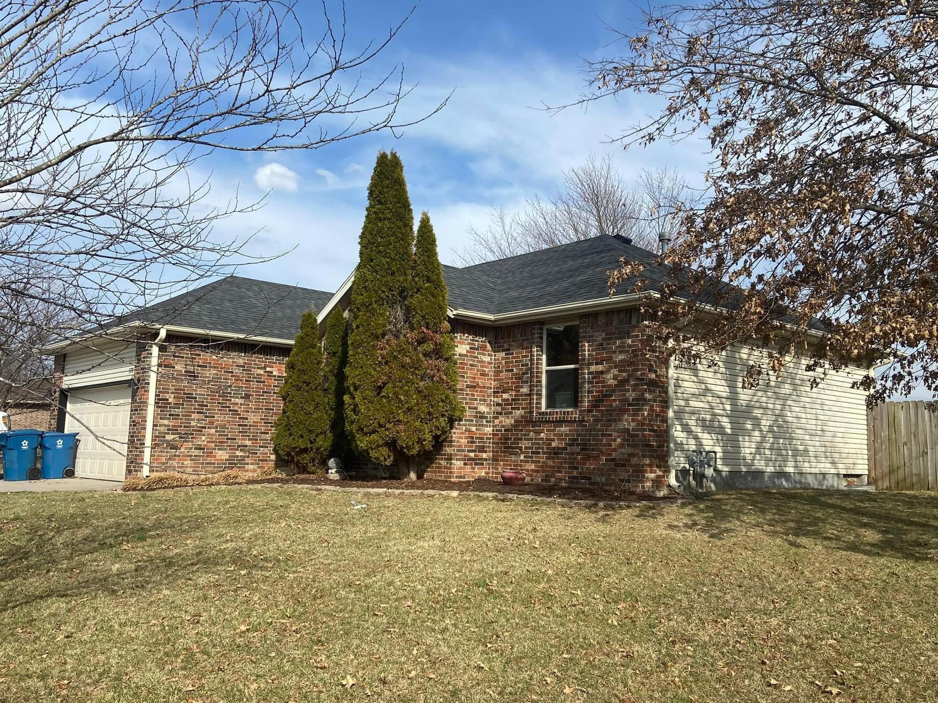 A brick house with a black roof and a lot of grass in front of it.